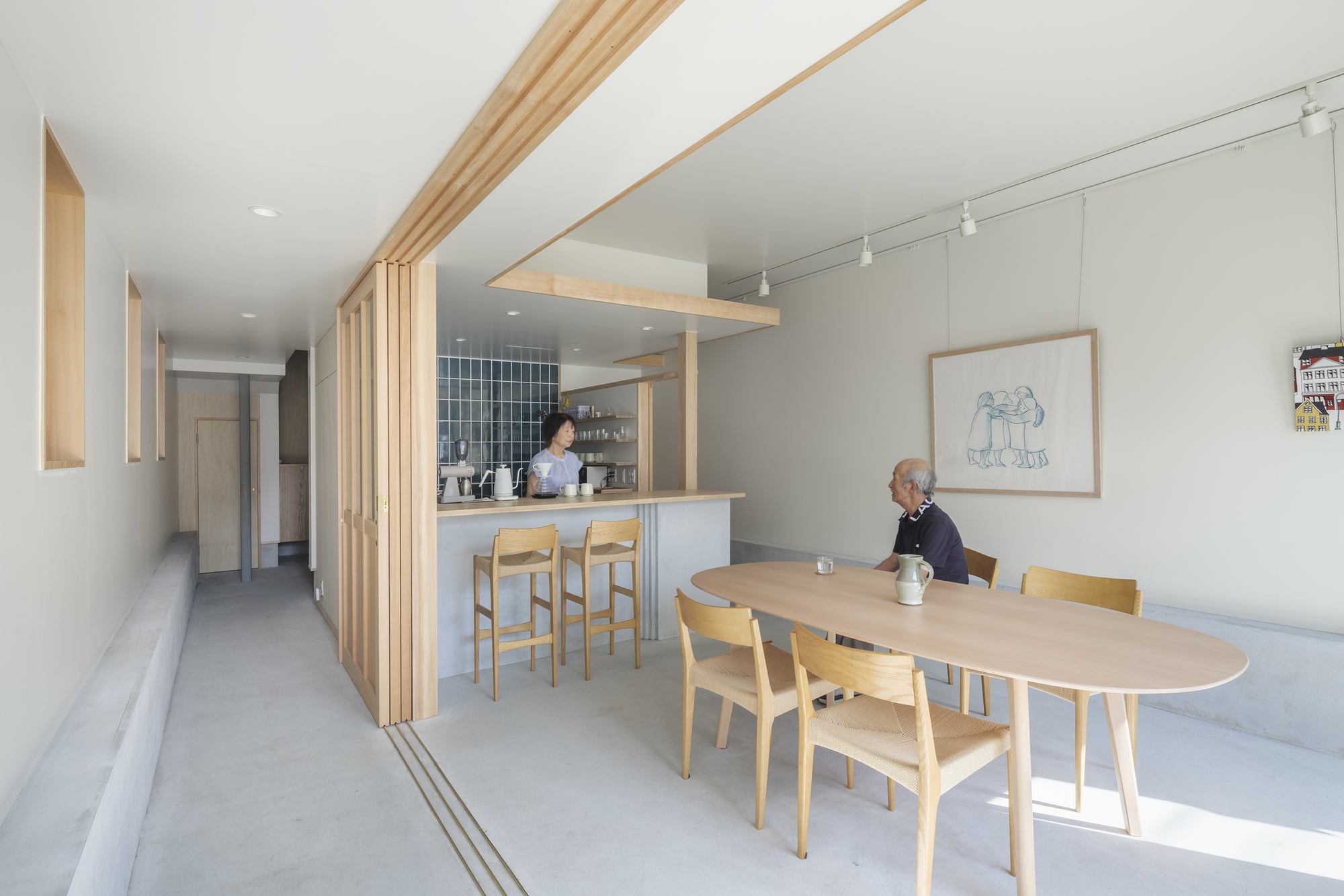 Open kitchen with timber slat partition and dining table where two residents sit and stand