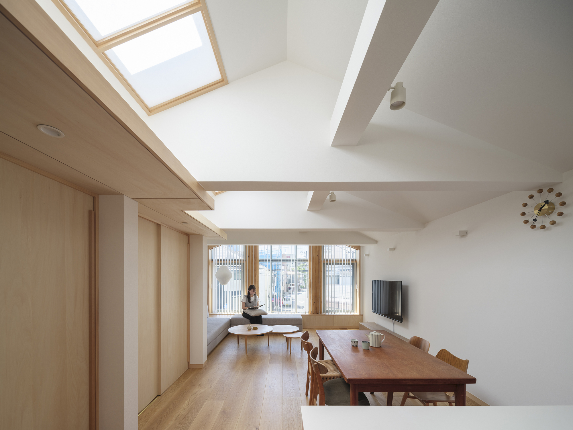 Open living space with timber-framed skylights and a seated figure by the window