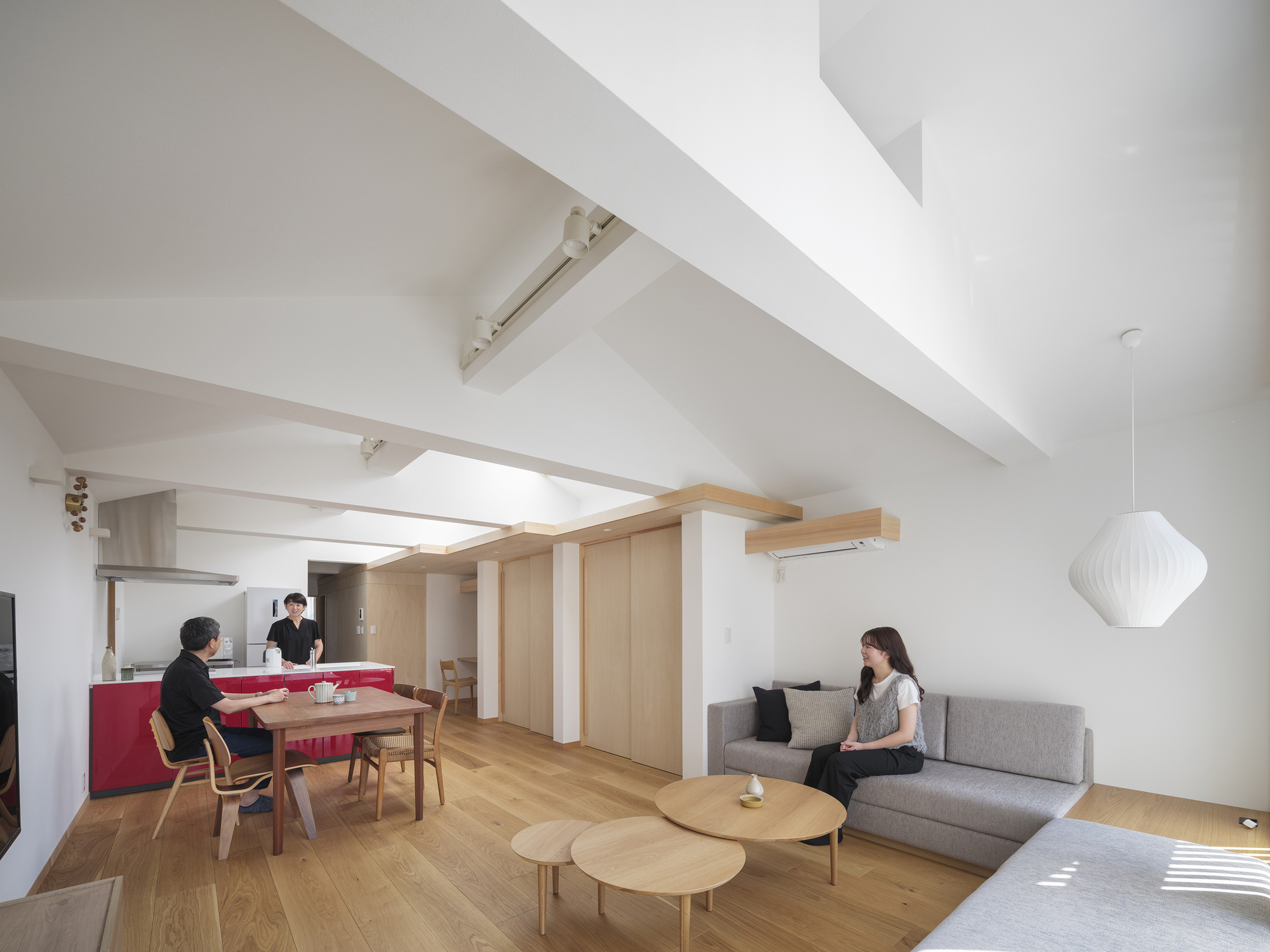 Open-plan living space with residents at dining table and kitchen under angled skylight