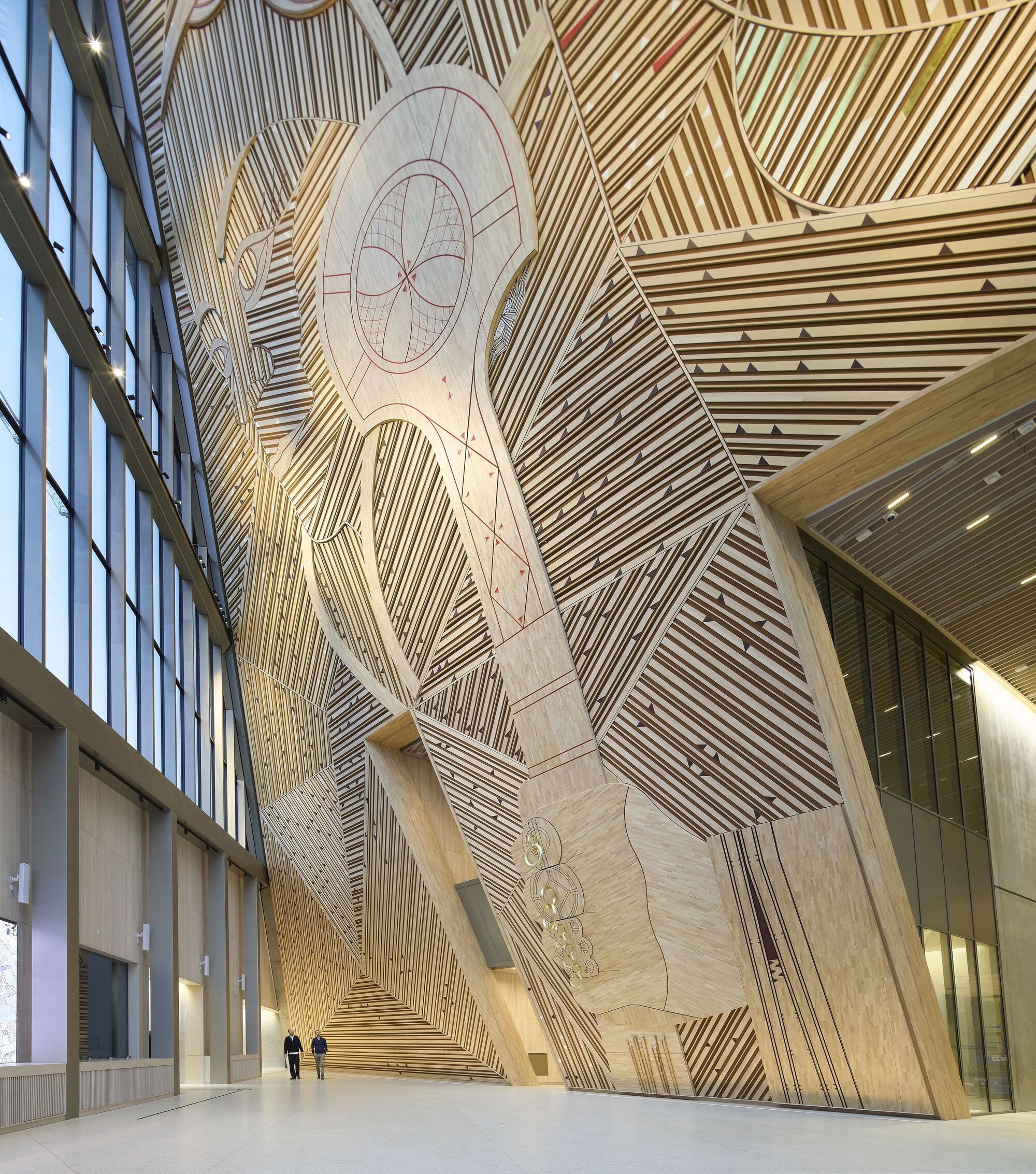 Towering atrium wall clad in wood slats arranged in diagonal patterns with carved figural reliefs