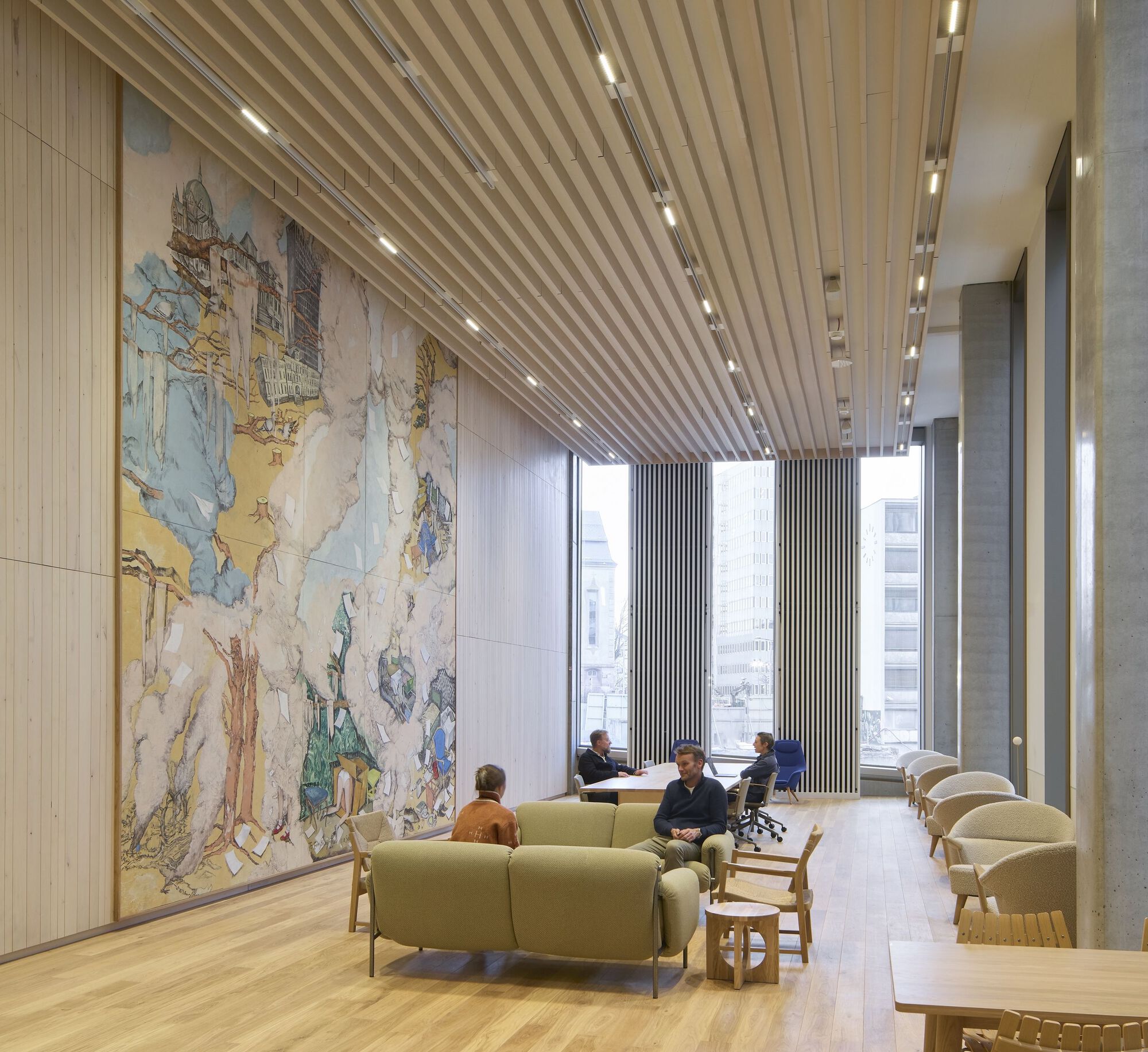 Lounge space with large tapestry wall hanging and green seating under diagonal wood slat ceiling