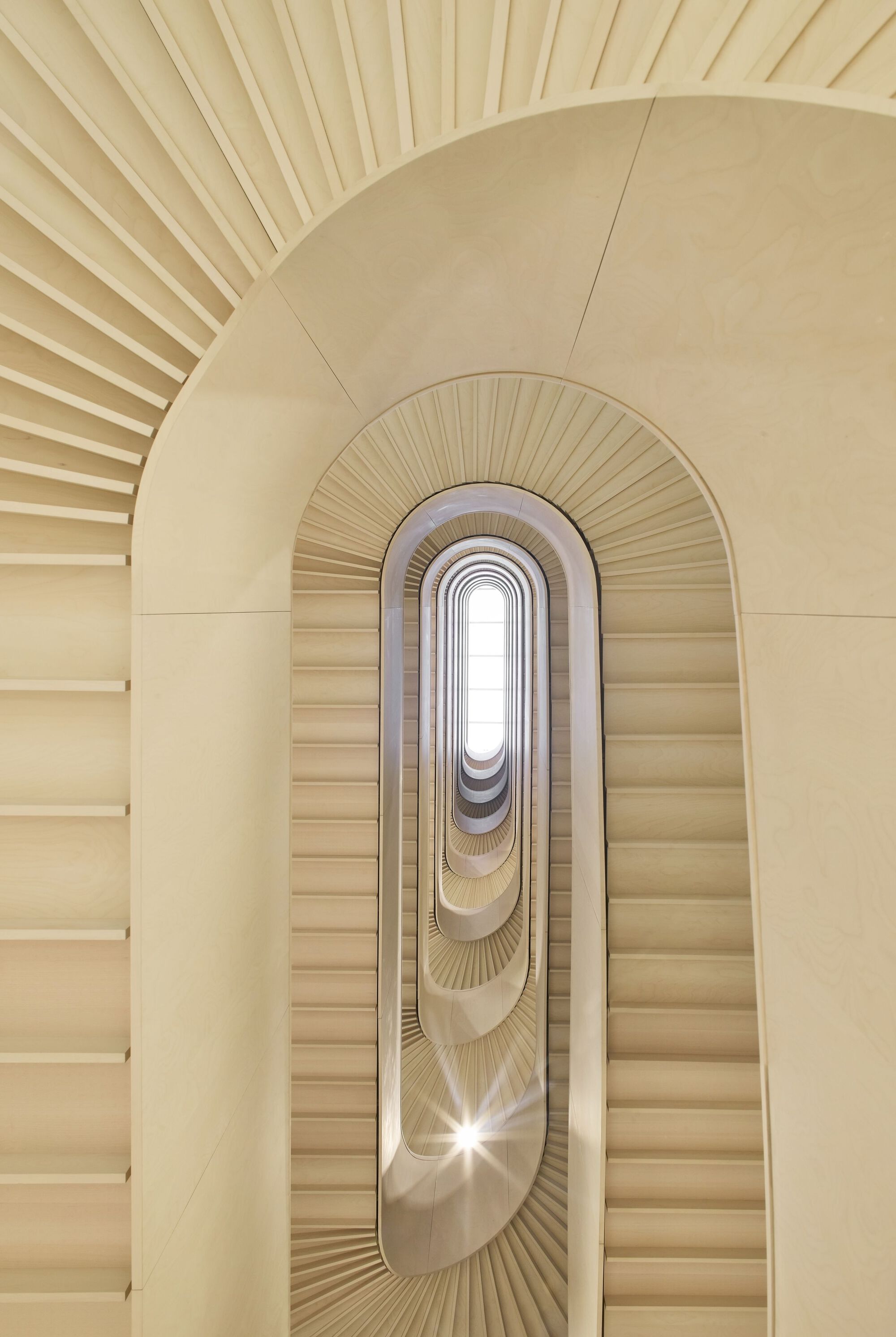 Upward view through oval stairwell with radiating handrails and skylight at summit creating bright central glow