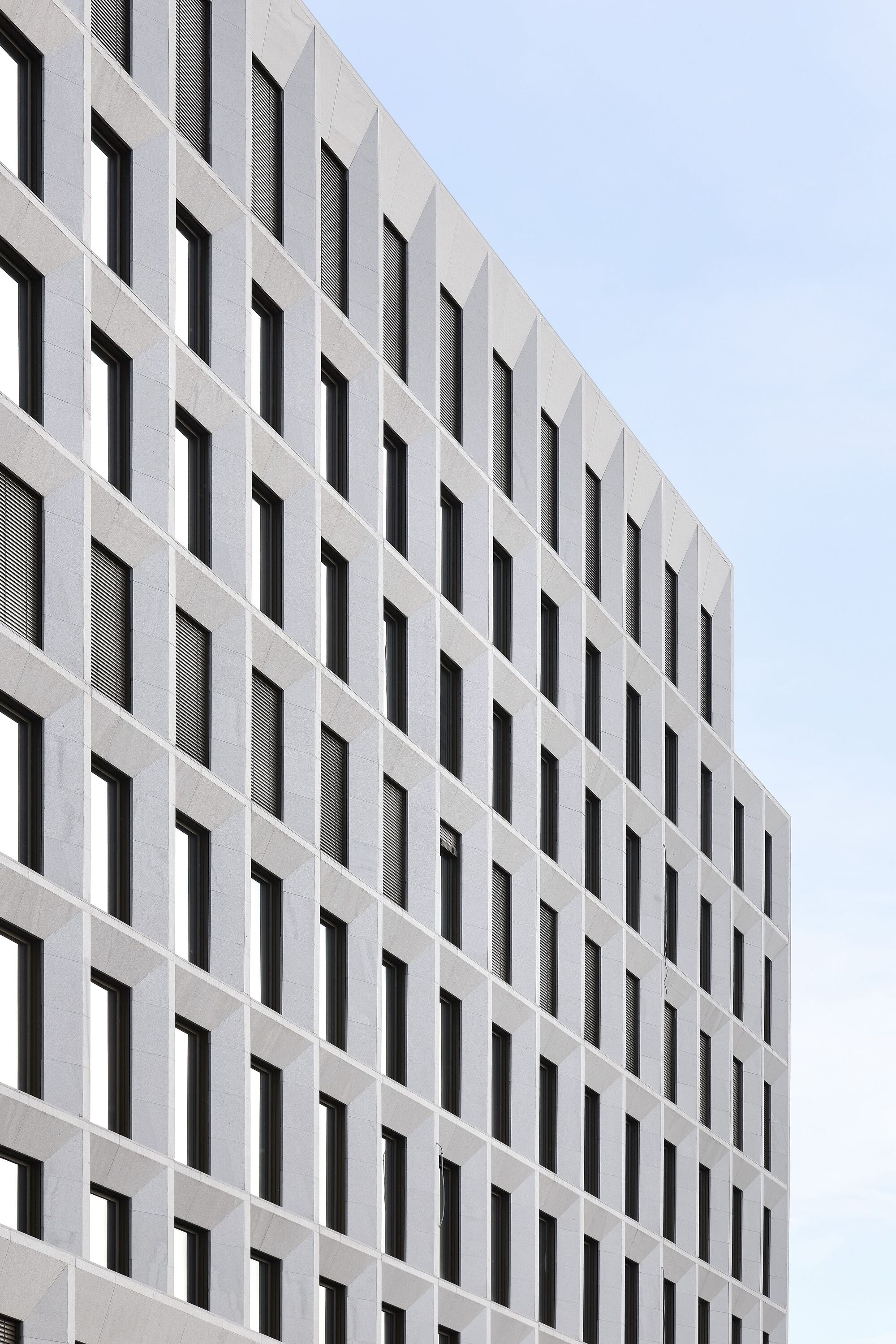 White precast concrete facade with rhythmic pattern of deep-set rectangular window openings under overcast sky