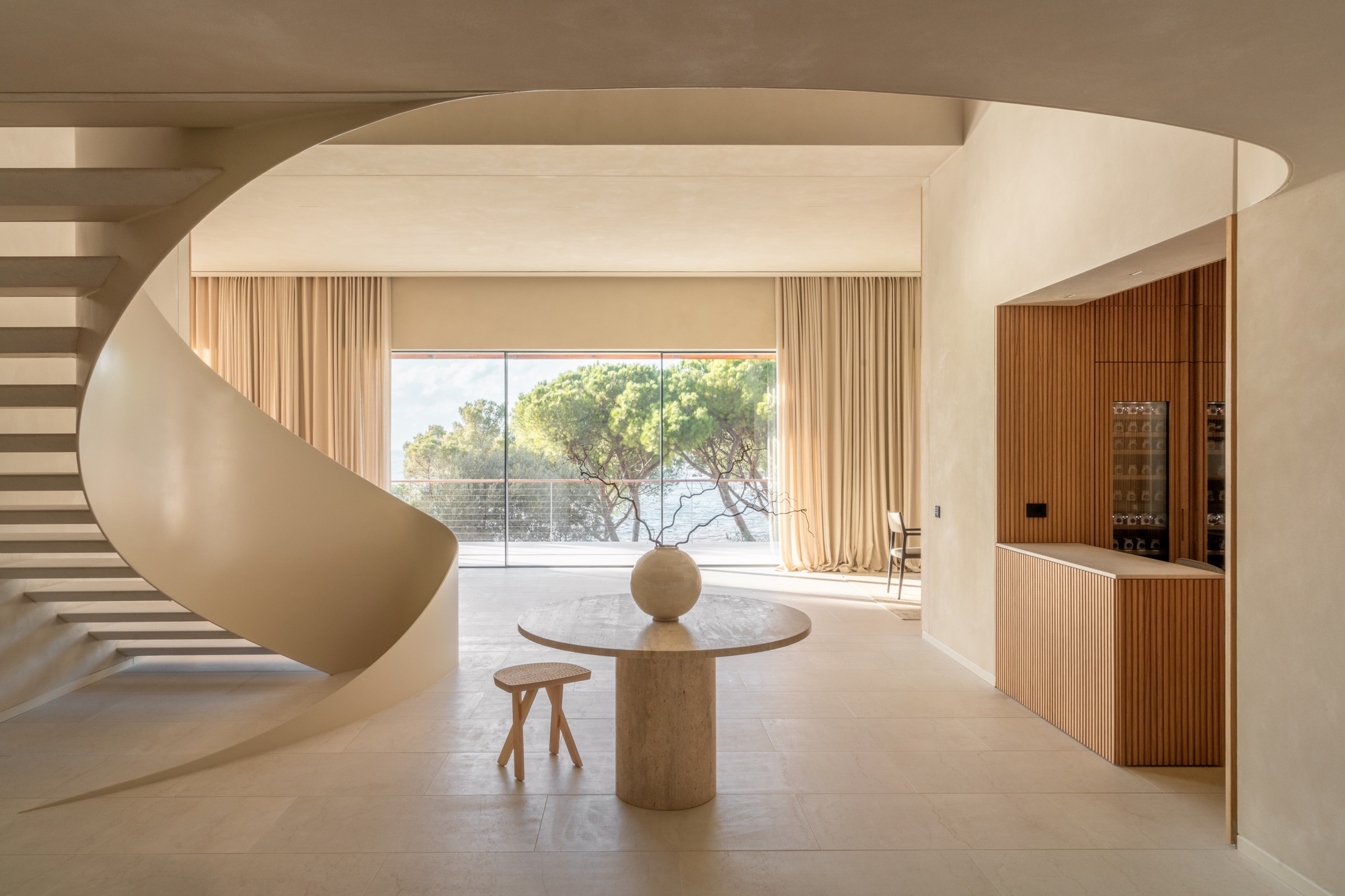 Interior entry hall with curved spiral staircase and slatted wood cabinetry framing a view to trees outside