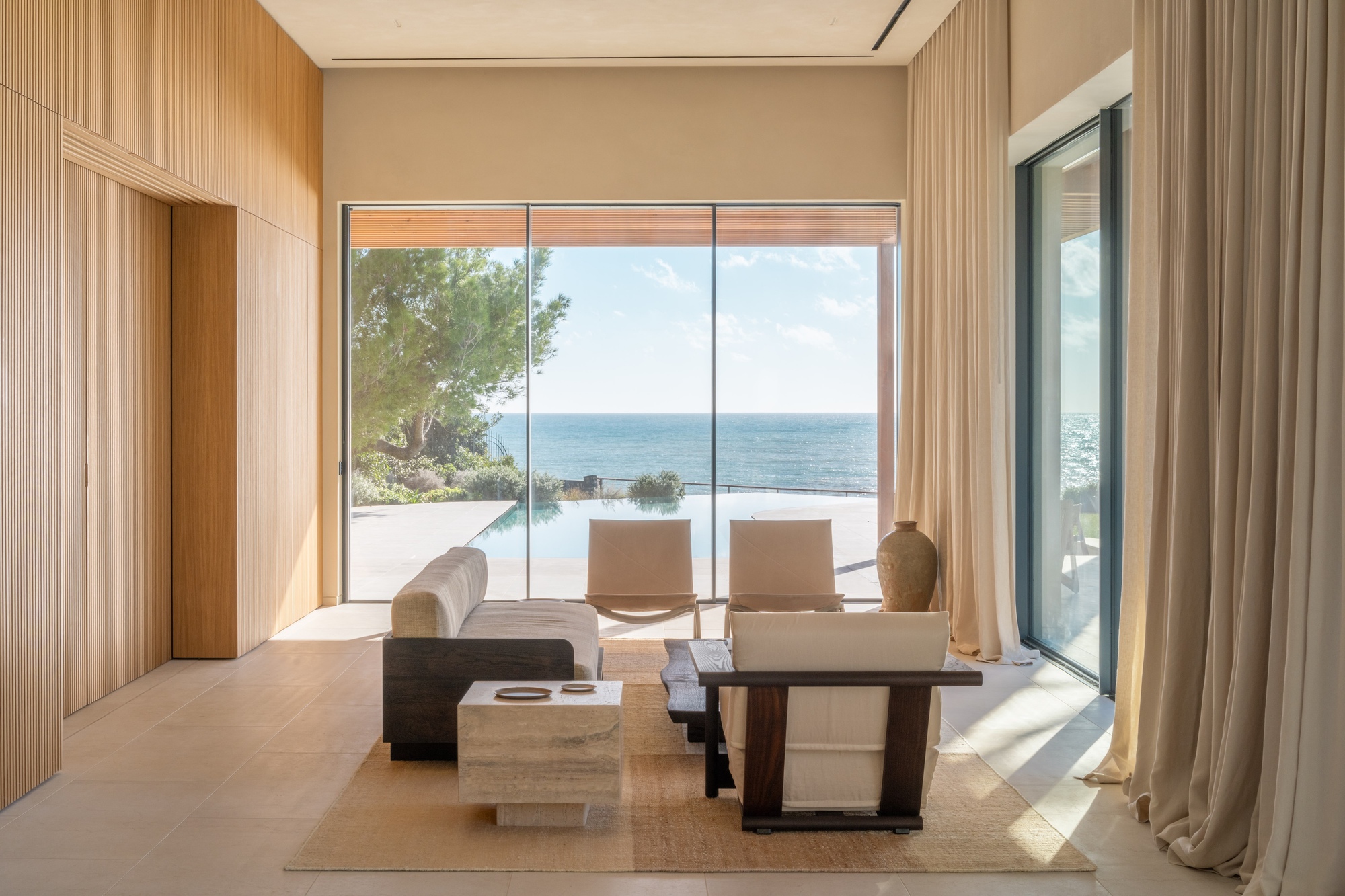 Living room framed by wood paneling with full-height glazing opening to a terrace and ocean view