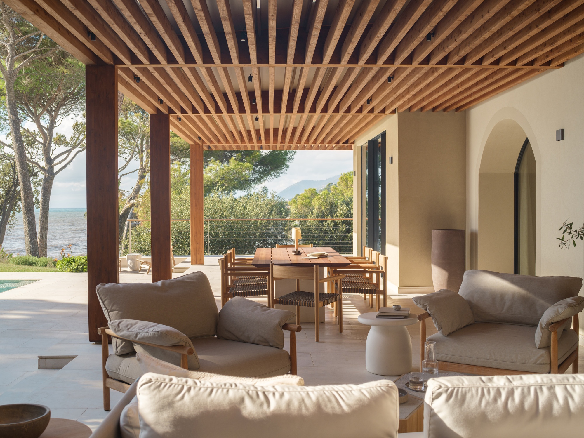 Covered terrace with timber slat ceiling and arched doorway framing the coastal landscape