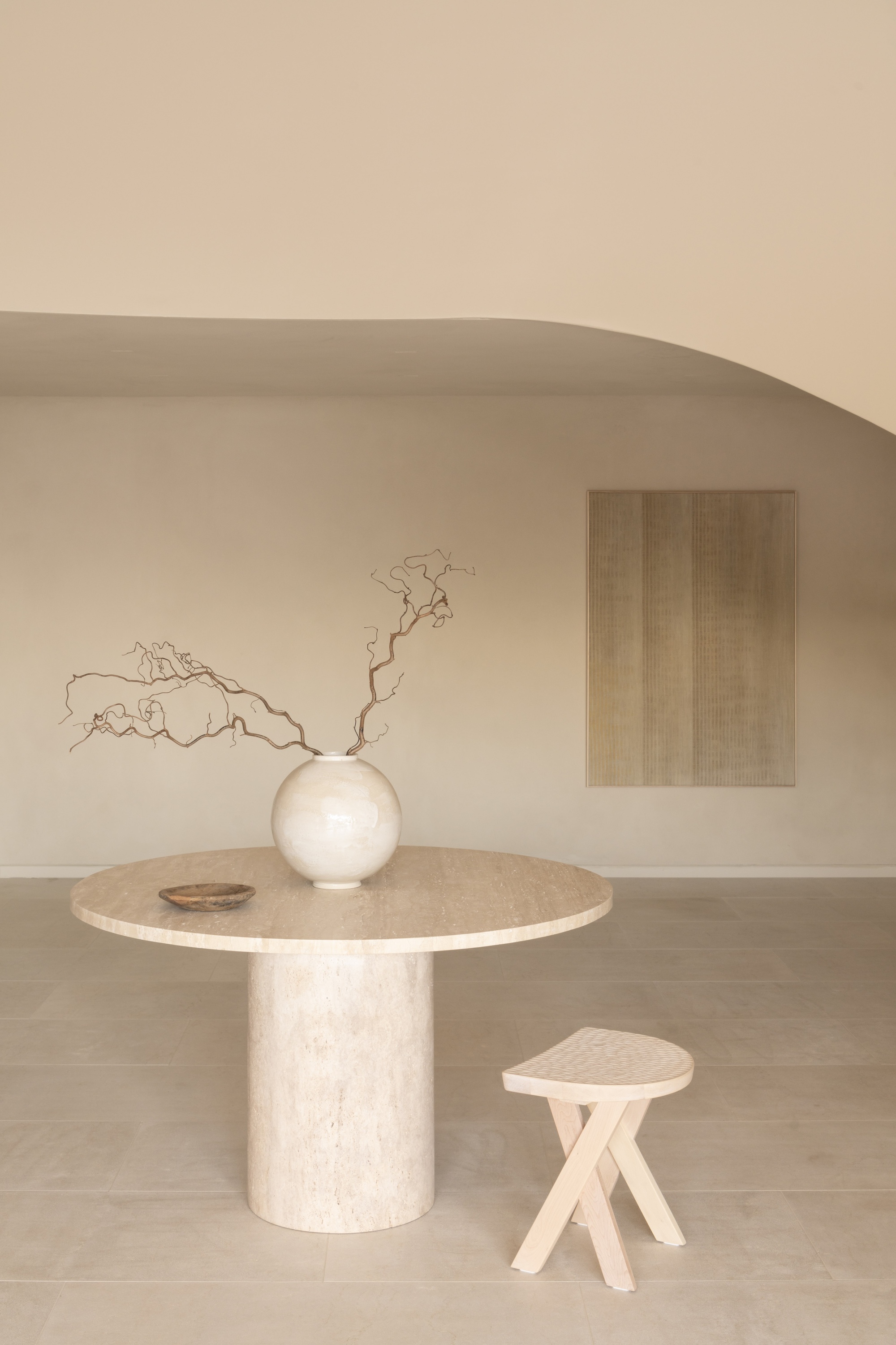 Travertine dining table with spherical vase and dried branches beneath a curved plaster ceiling