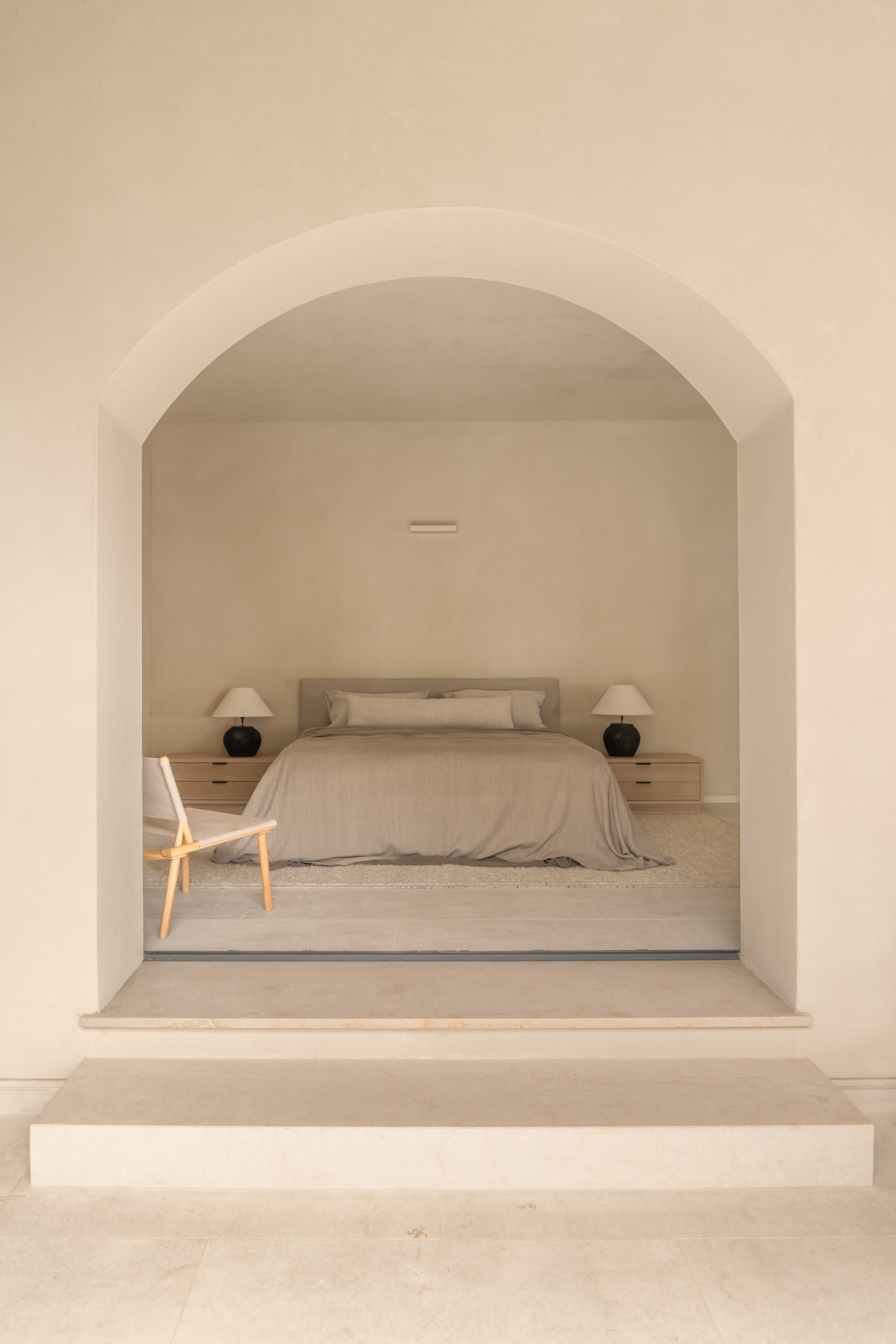 Arched doorway framing a bedroom with stepped threshold and pale stone floor