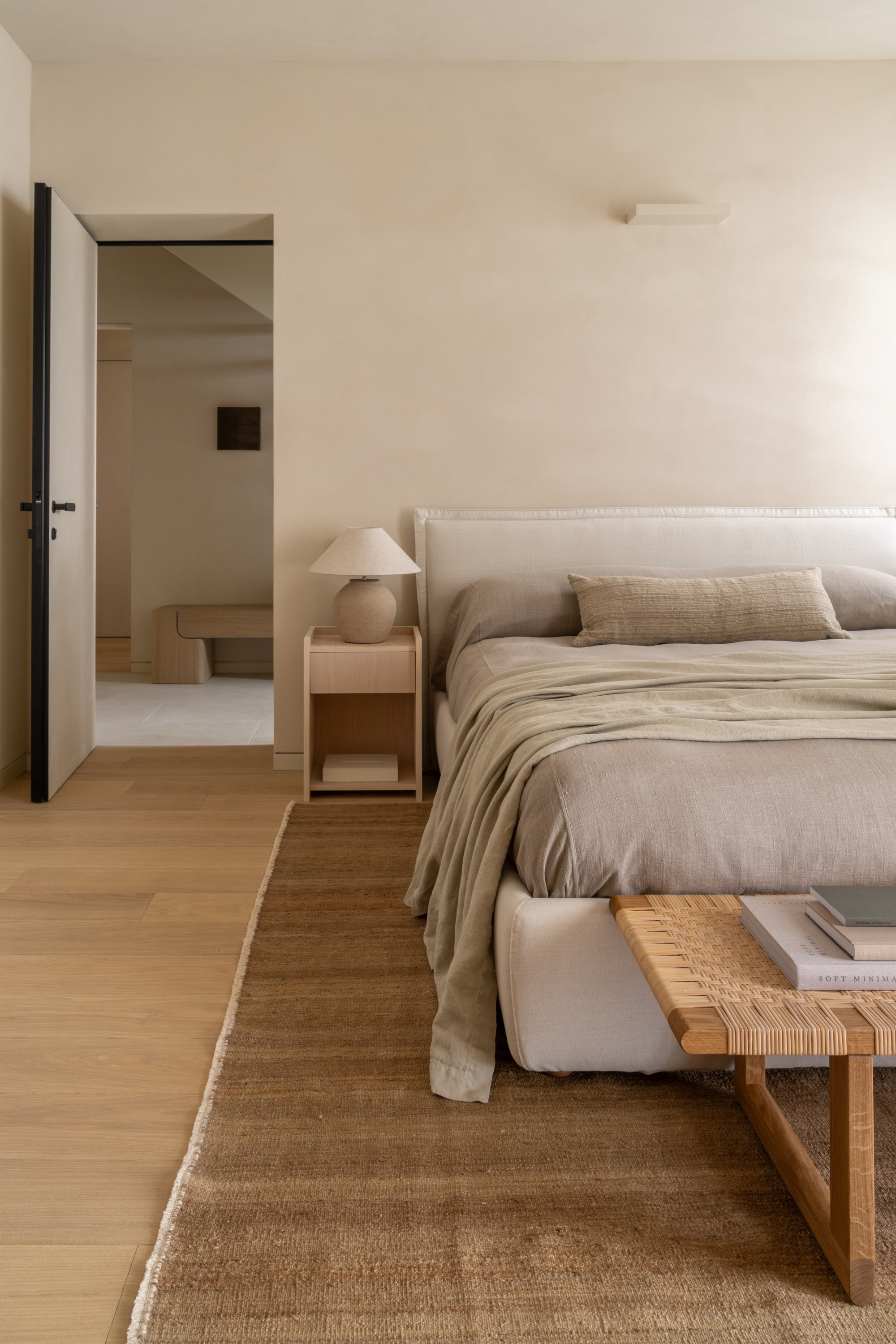 Bedroom with oak flooring and open door revealing a minimalist hallway beyond