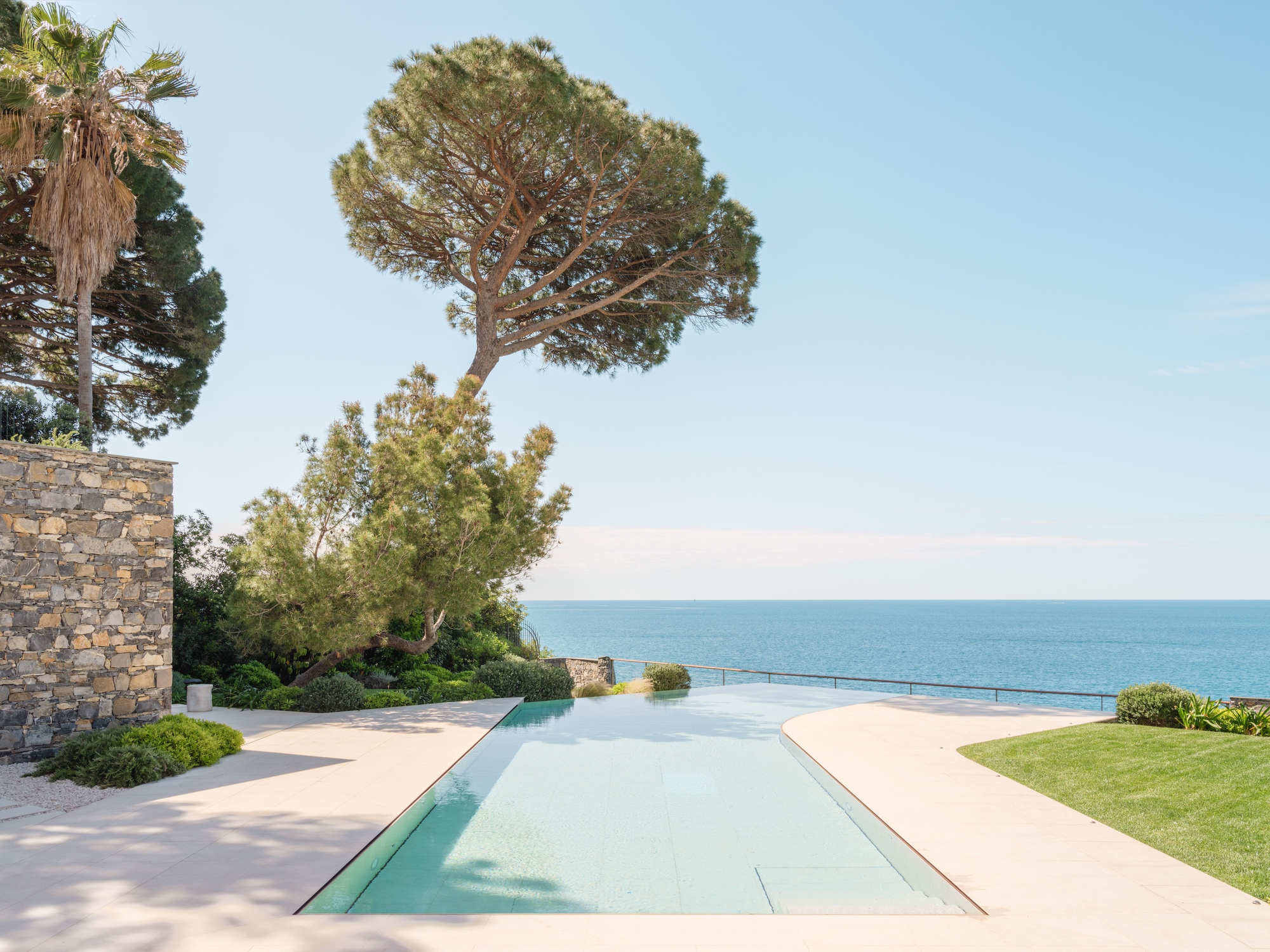 Rectangular pool channel set into pale paving with garden and sea horizon beyond