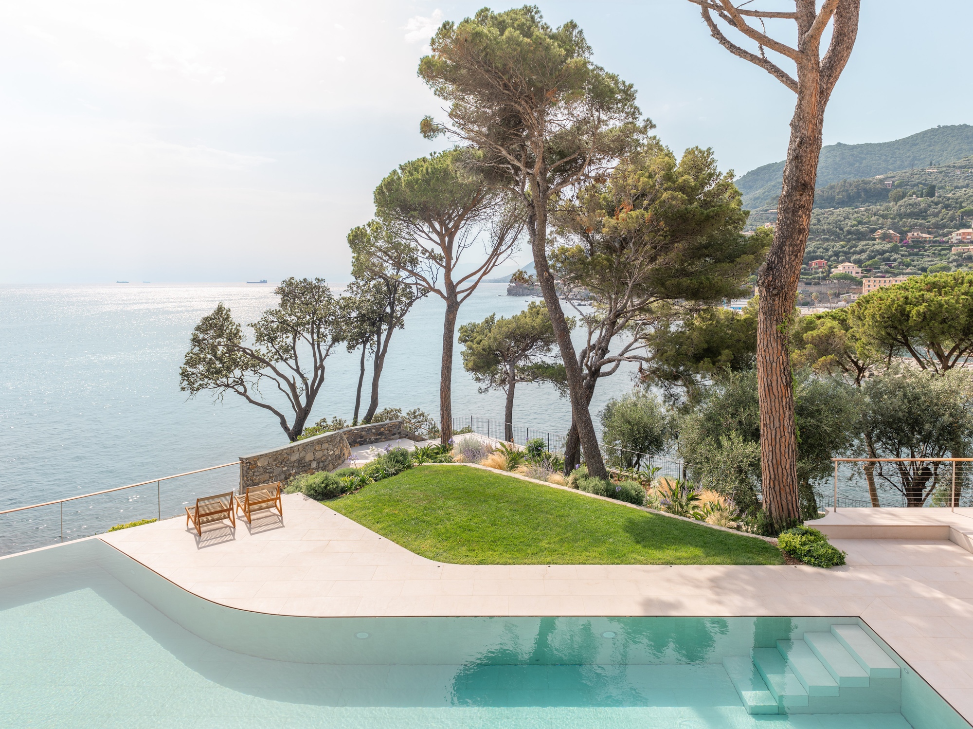 Curved infinity pool edge with lawn and mature pine trees overlooking the sea