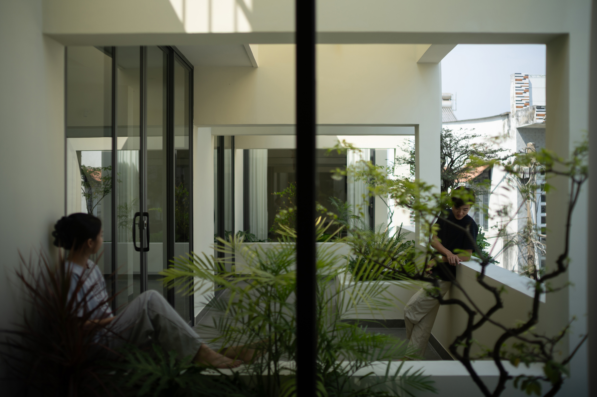 Interior courtyard glimpsed through glass doors with two residents and planted palms in filtered light