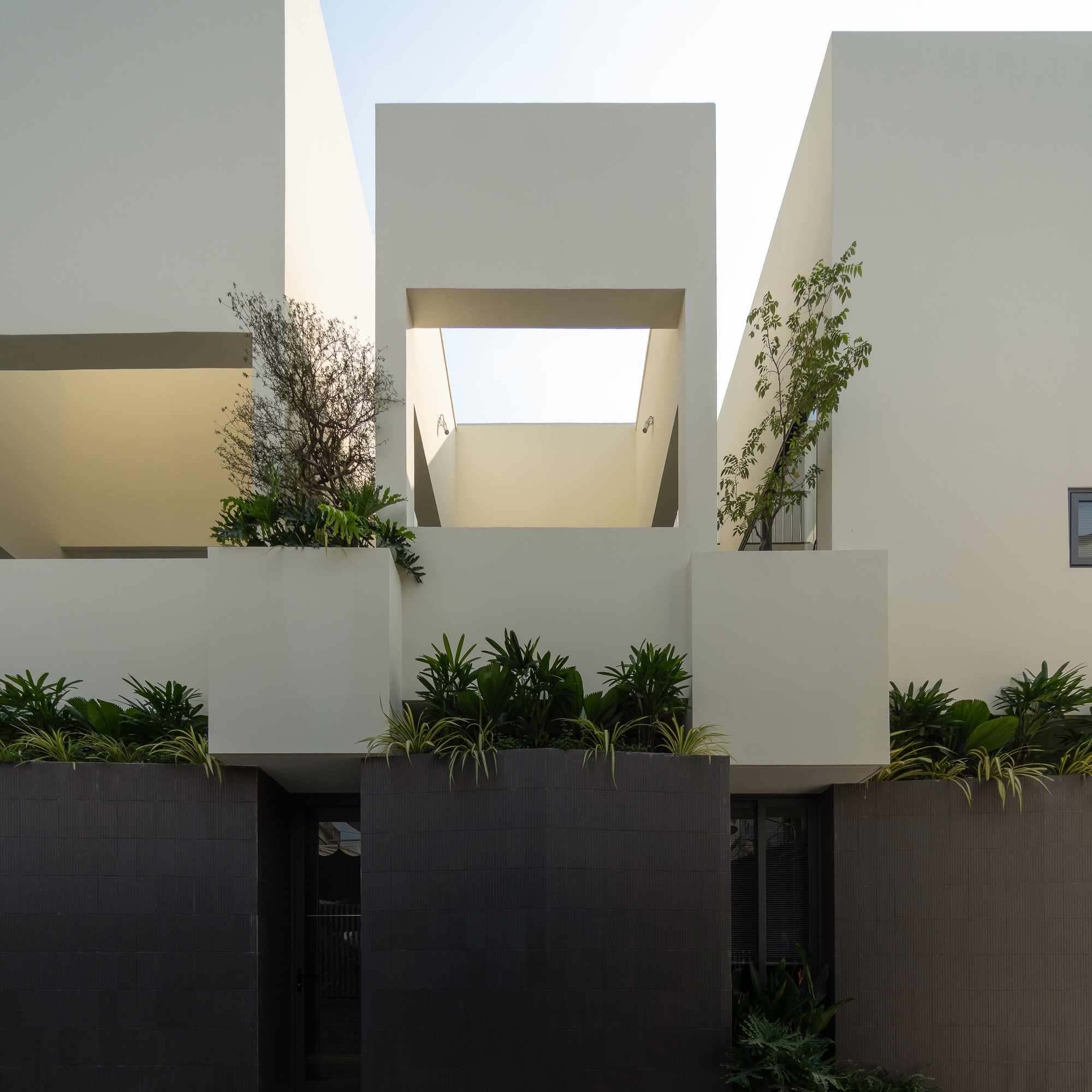 Street view of stacked white volumes with planted terraces above a dark tiled base at dusk