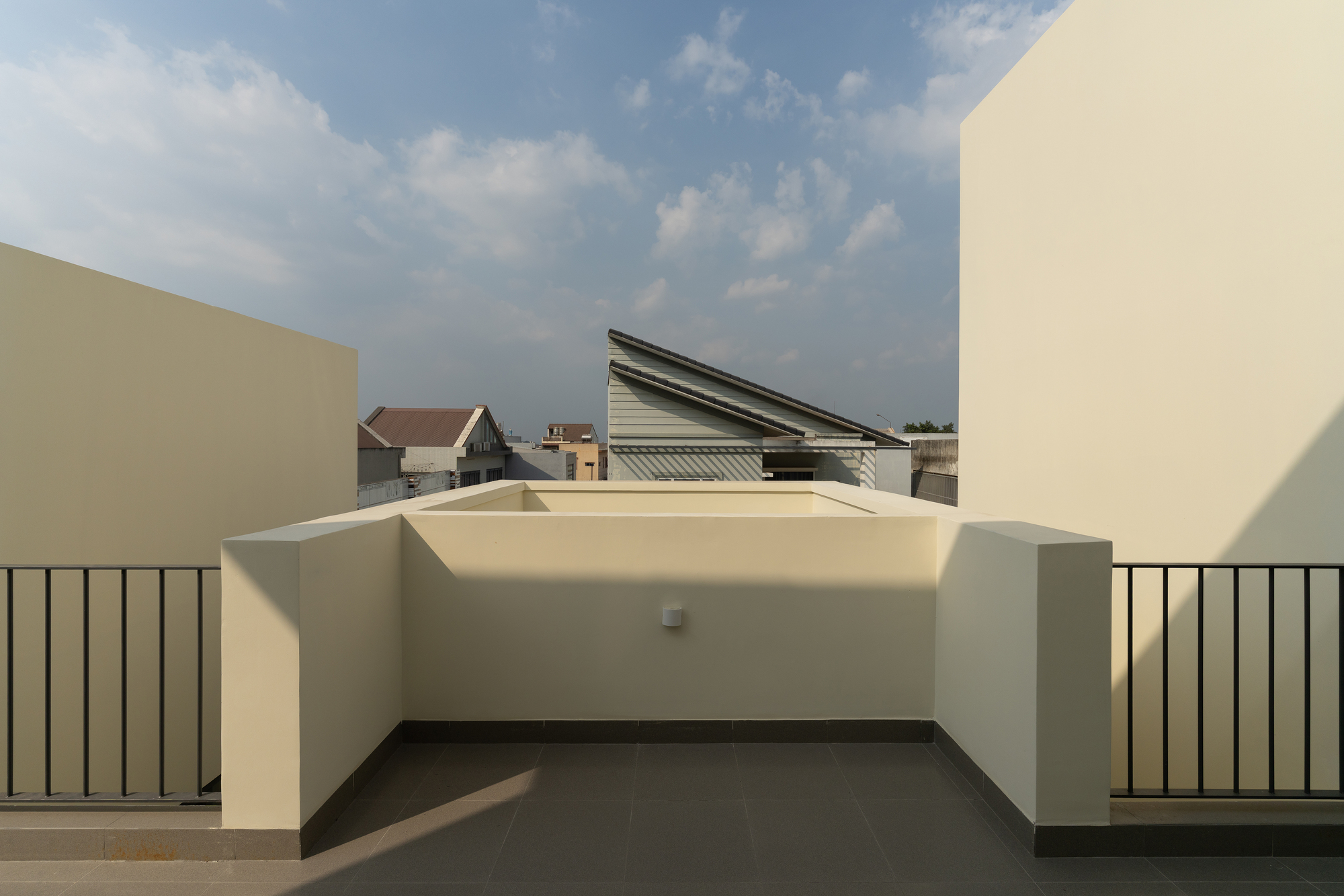 Rooftop terrace with cream-colored parapet walls and metal railing under an afternoon sky