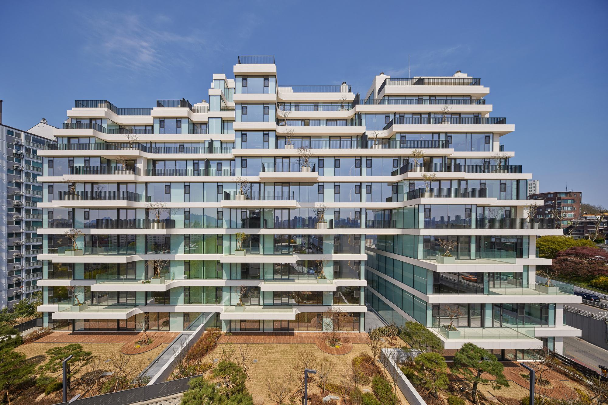 Facade of stepped balconies with glass railings overlooking a newly planted courtyard with young trees