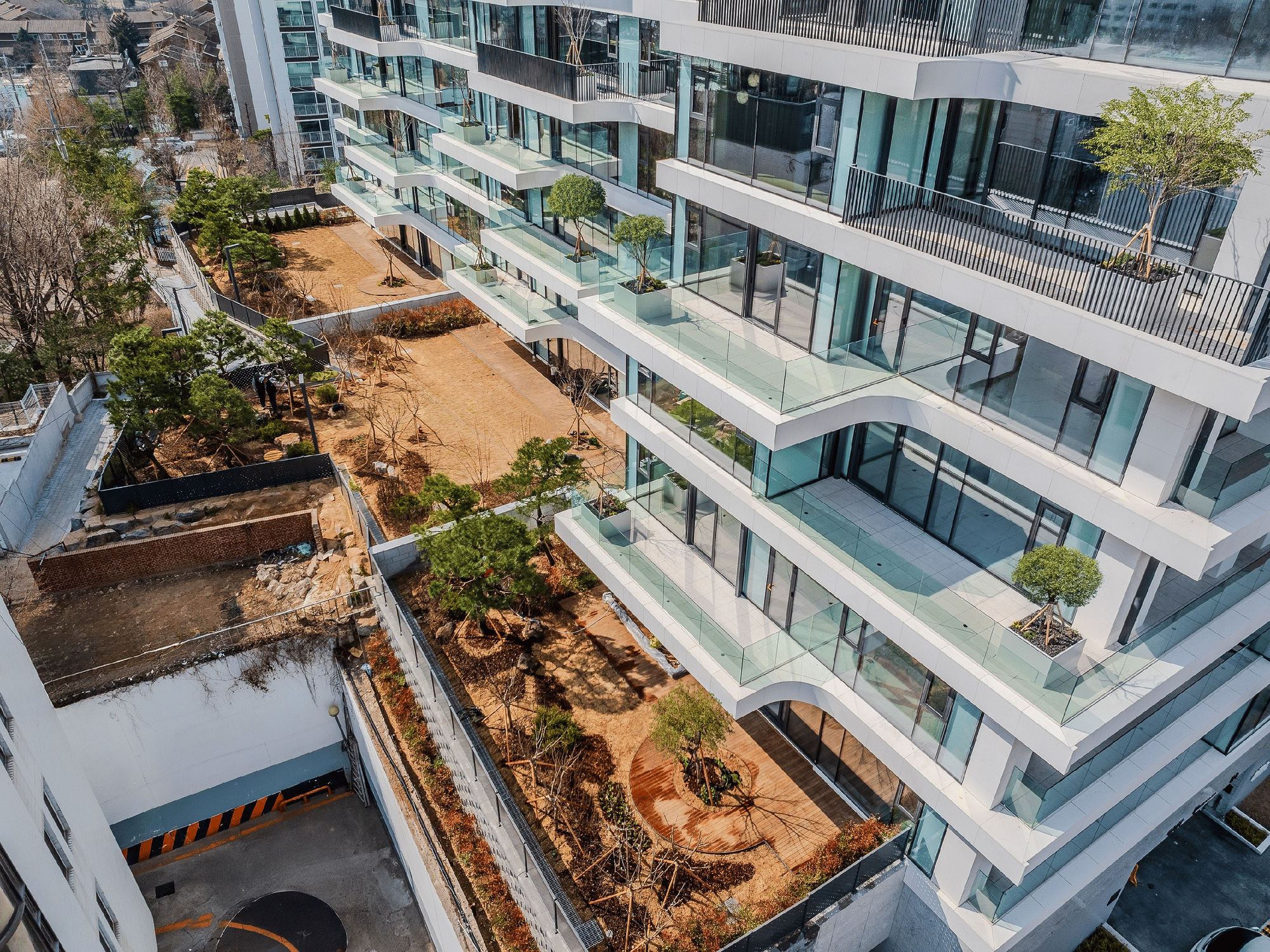 Aerial view of terraced courtyards with fresh soil, planted beds, and glass-edged balconies between buildings
