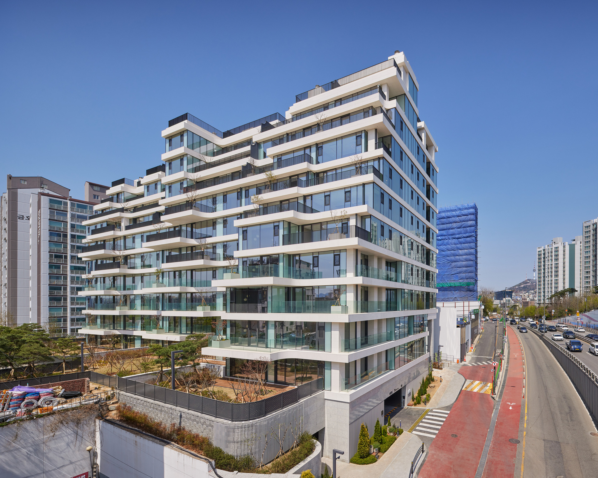 Street corner view showing the offset white balconies and glazed facade beside a roadway with traffic
