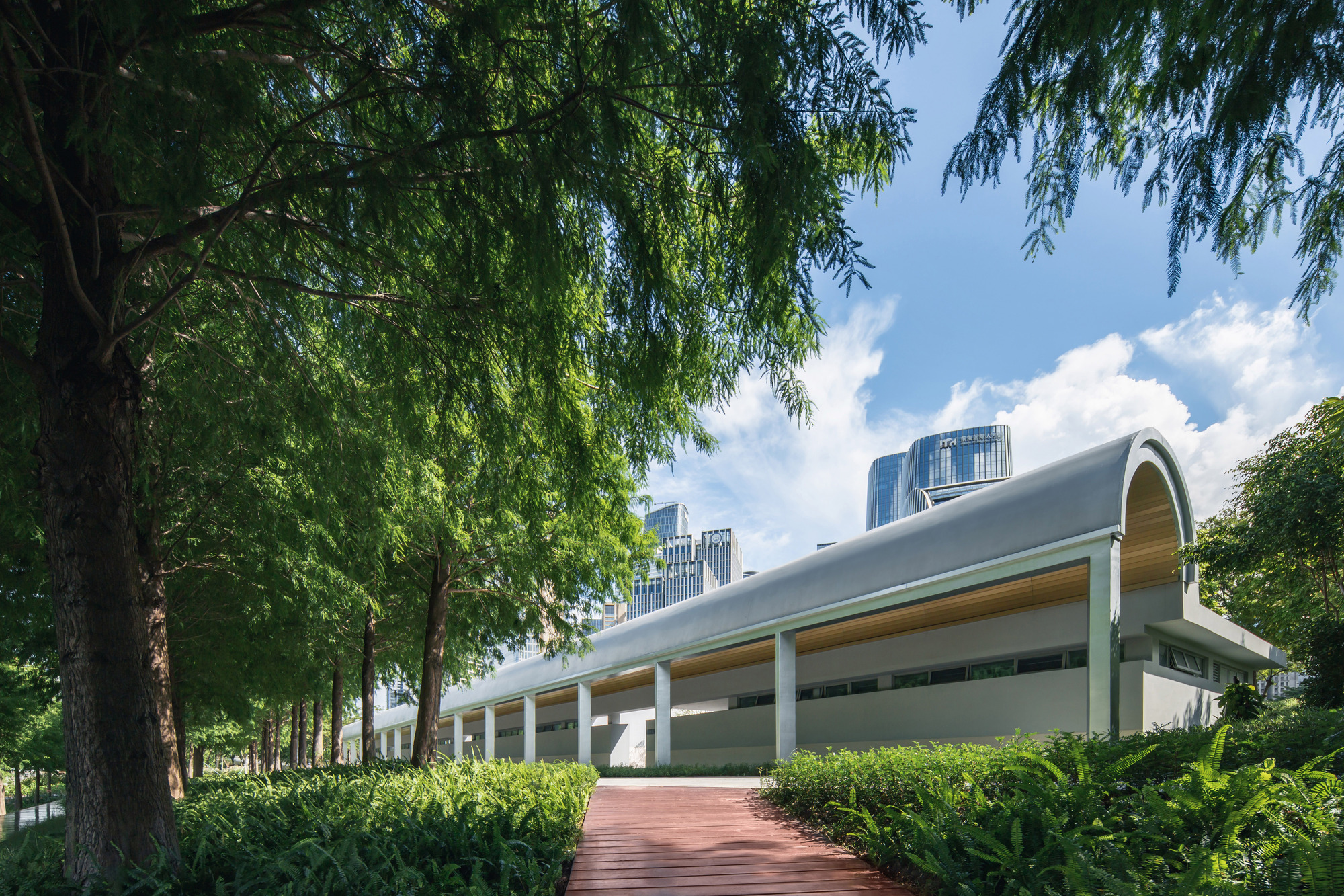 Barrel-vaulted roof above a colonnade entry plaza framed by willow trees and trimmed hedges