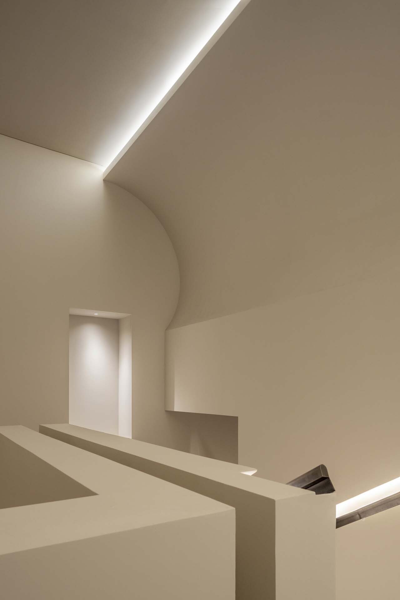 Stairwell with vaulted ceiling, recessed linear lighting and geometric white plaster volumes