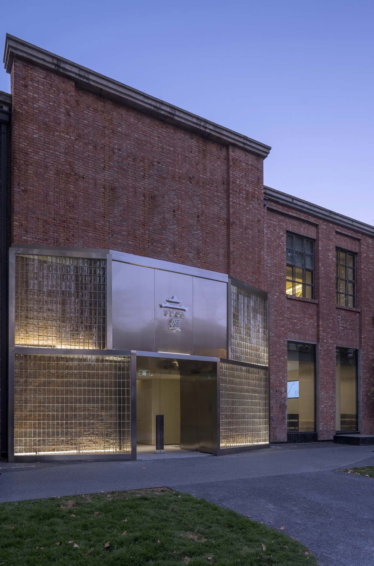 Brick facade with glass brick panels and illuminated entrance at dusk