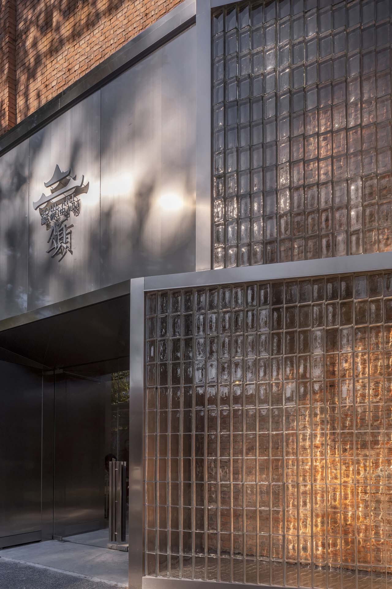 Street-level entrance with glass block facade and grey metal panel above bearing a sculpted logo