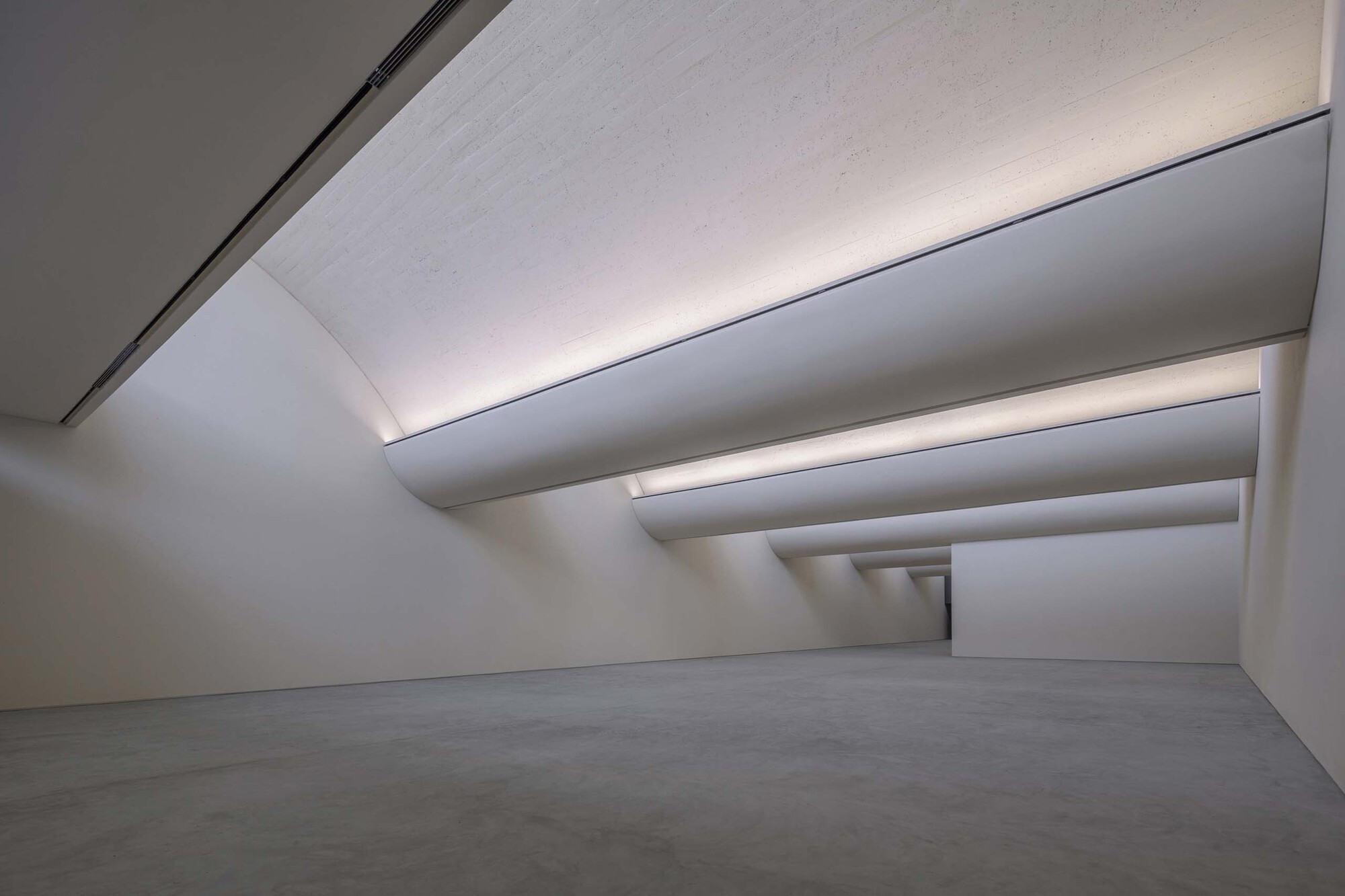 Interior gallery space with stepped ceiling planes creating receding layers of indirect light above polished floor