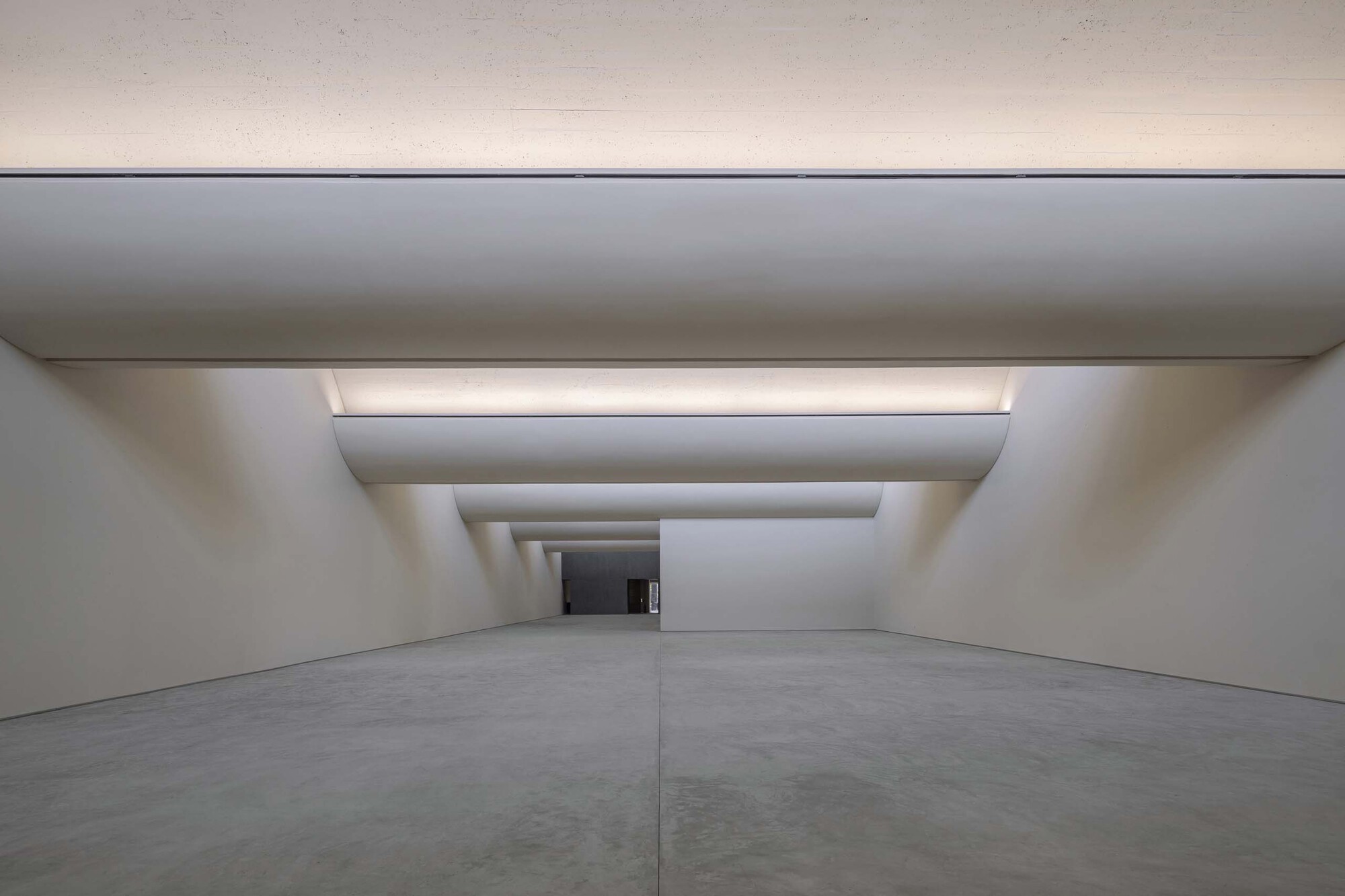 Gallery corridor with telescoping ceiling recesses and concealed lighting drawing the eye toward a distant opening