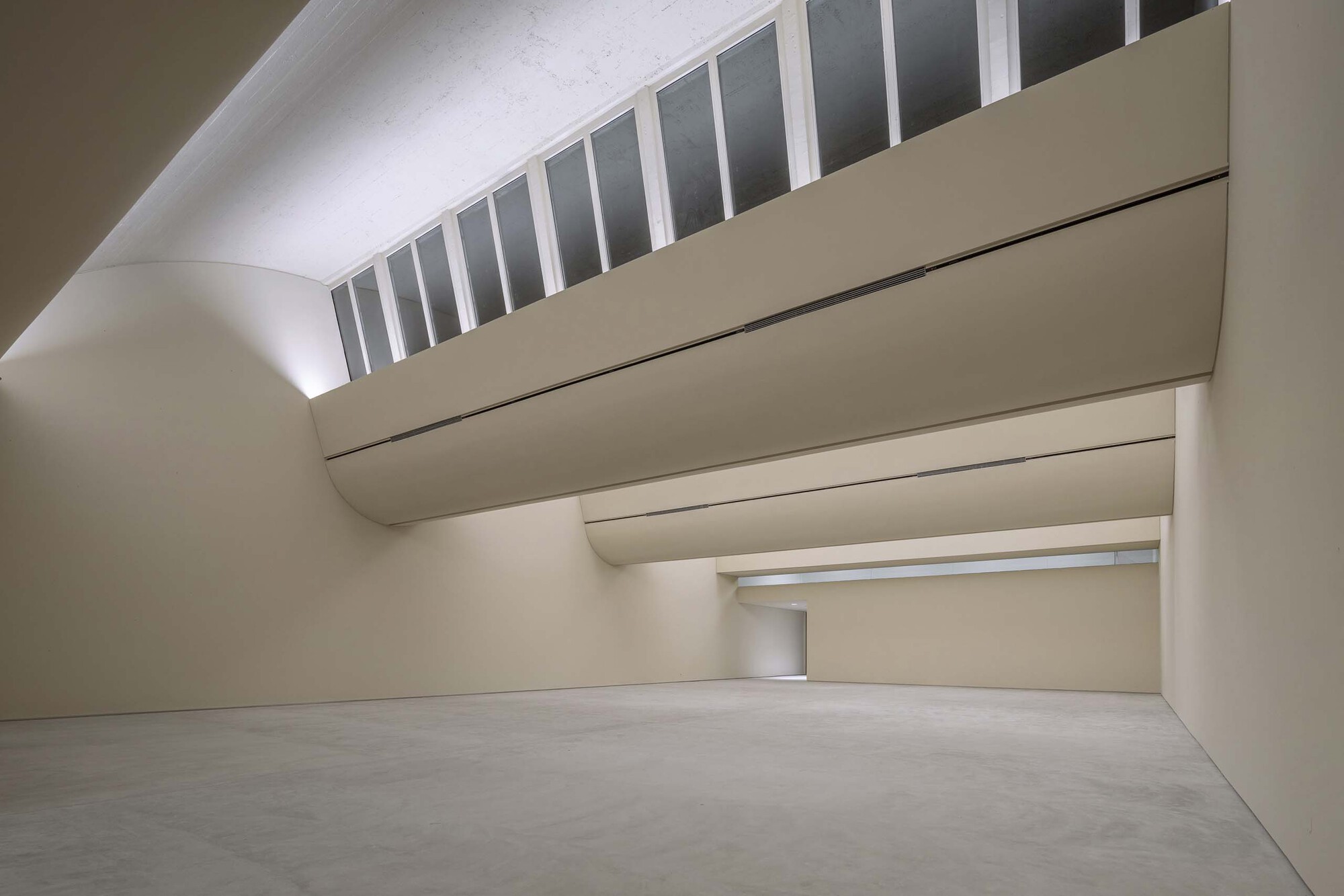 Gallery space with curved ceiling and horizontal clerestory admitting daylight above layered wall planes