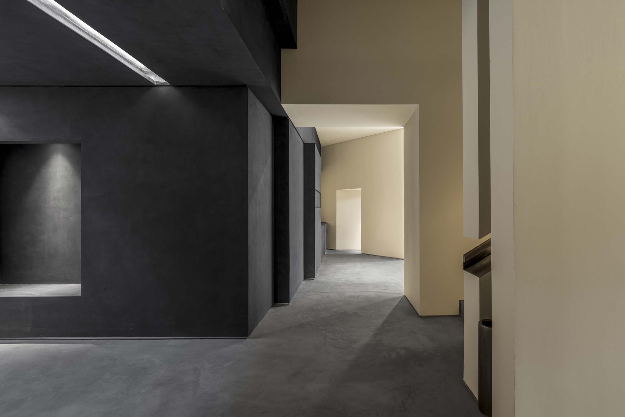 Circulation corridor between black metallic walls and cream partitions with polished concrete floor