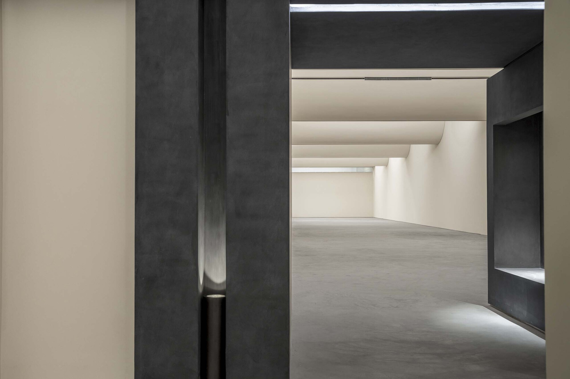 Doorway framed by dark concrete portal opening into a gallery space with recessed ceiling coves