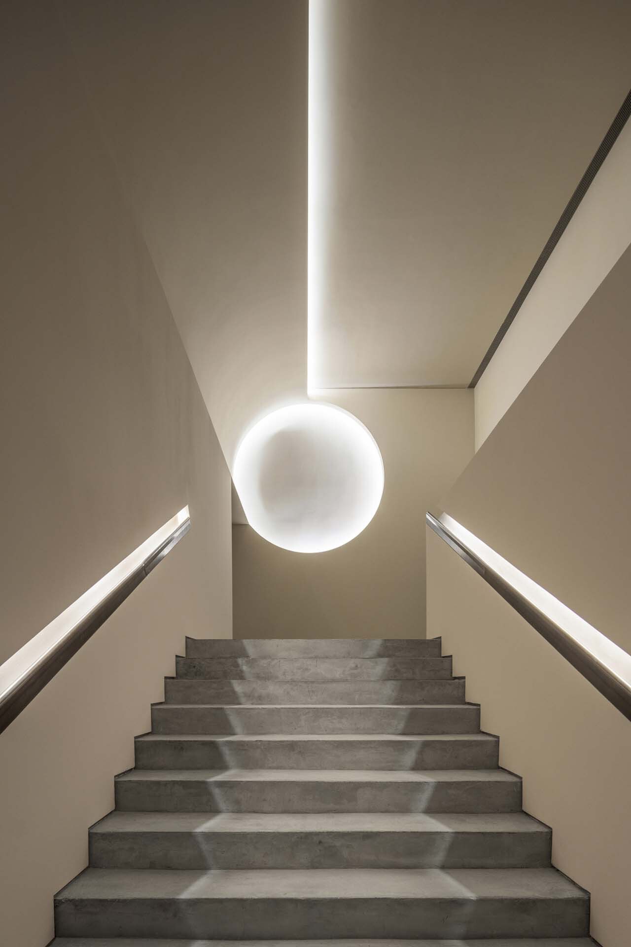 Upward view of concrete stair with spherical pendant light and illuminated ceiling slot above