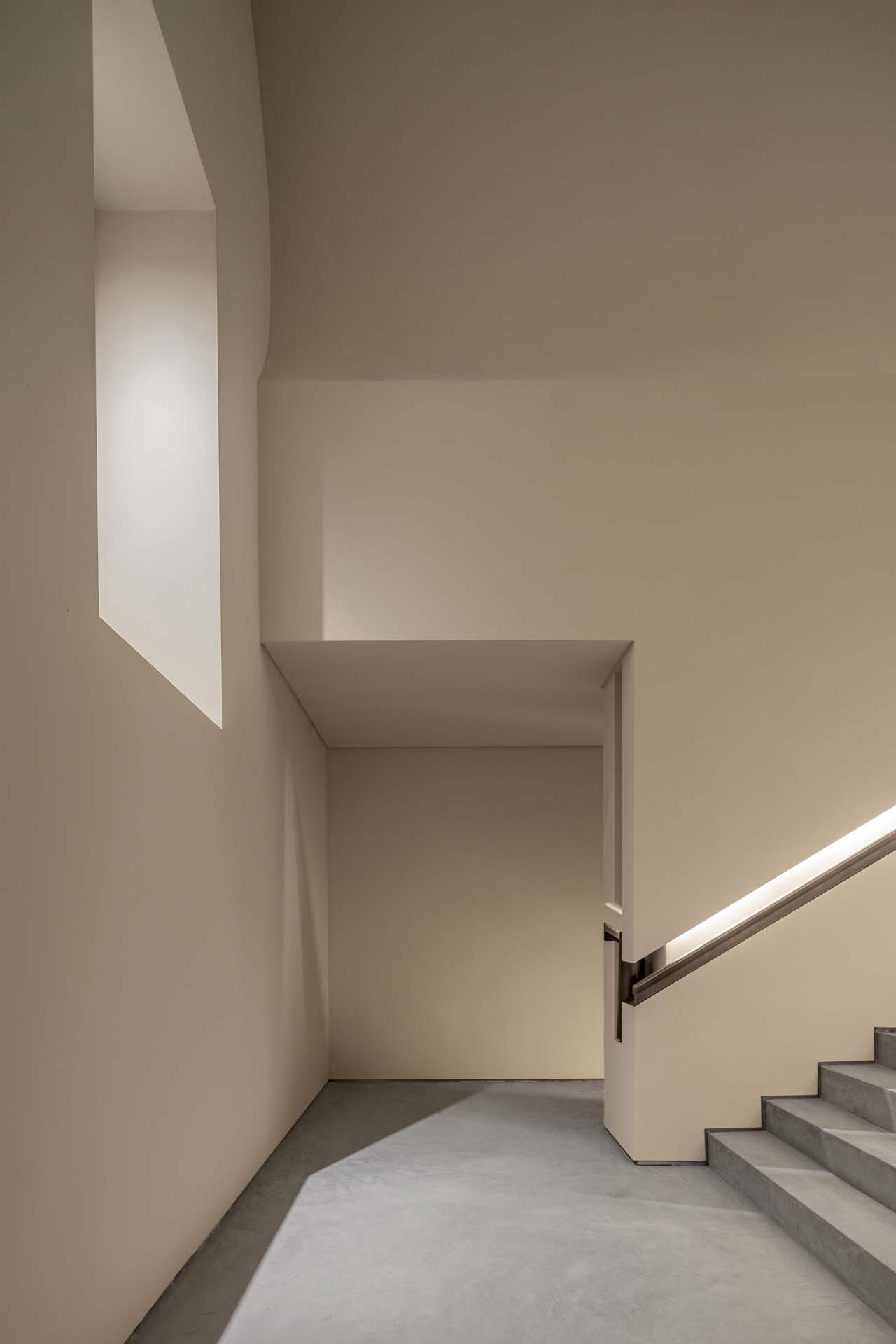 Stairwell landing with angled skylight casting morning light across the plaster walls and gray flooring