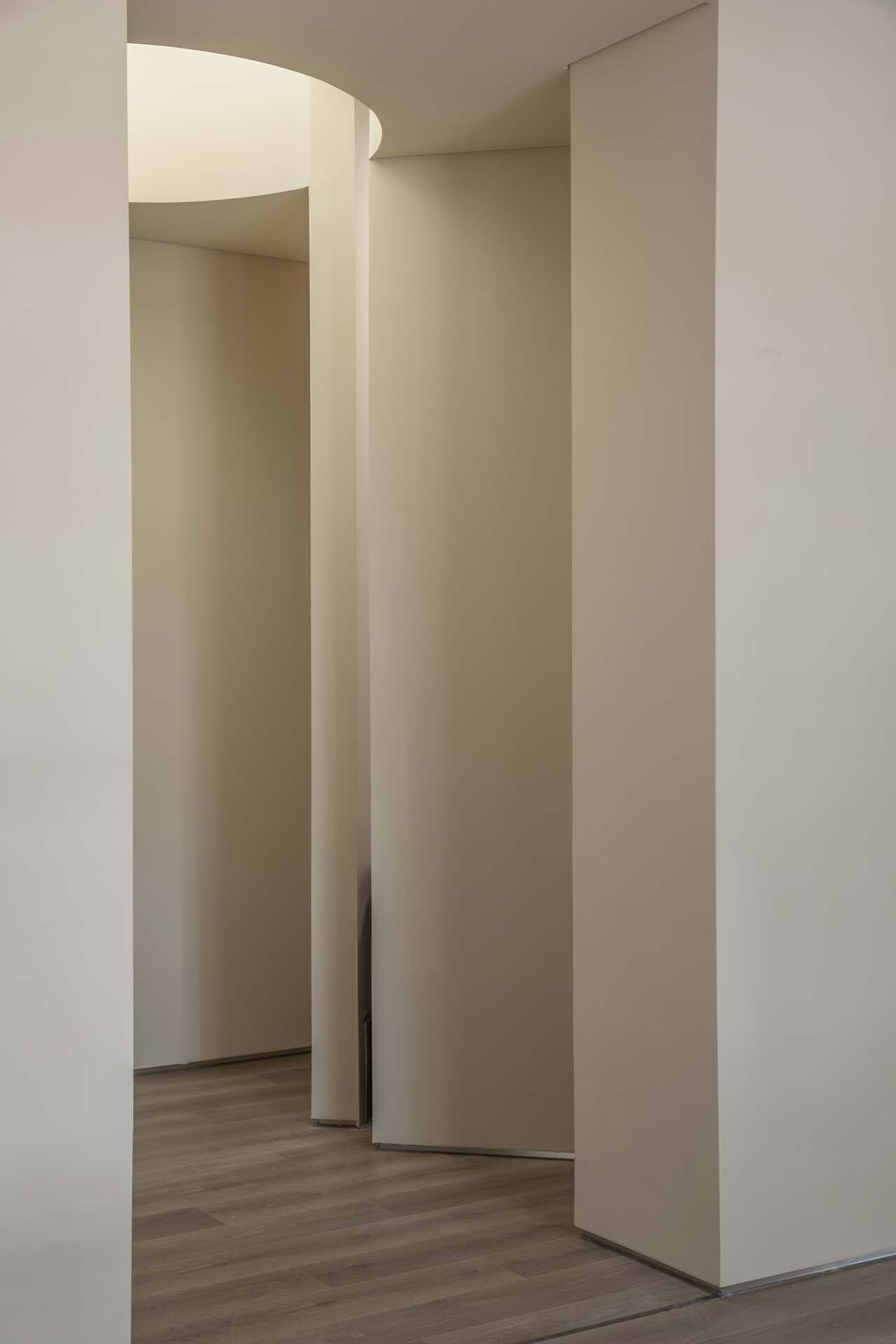 View through curving white partitions creating layered openings with pale wood flooring