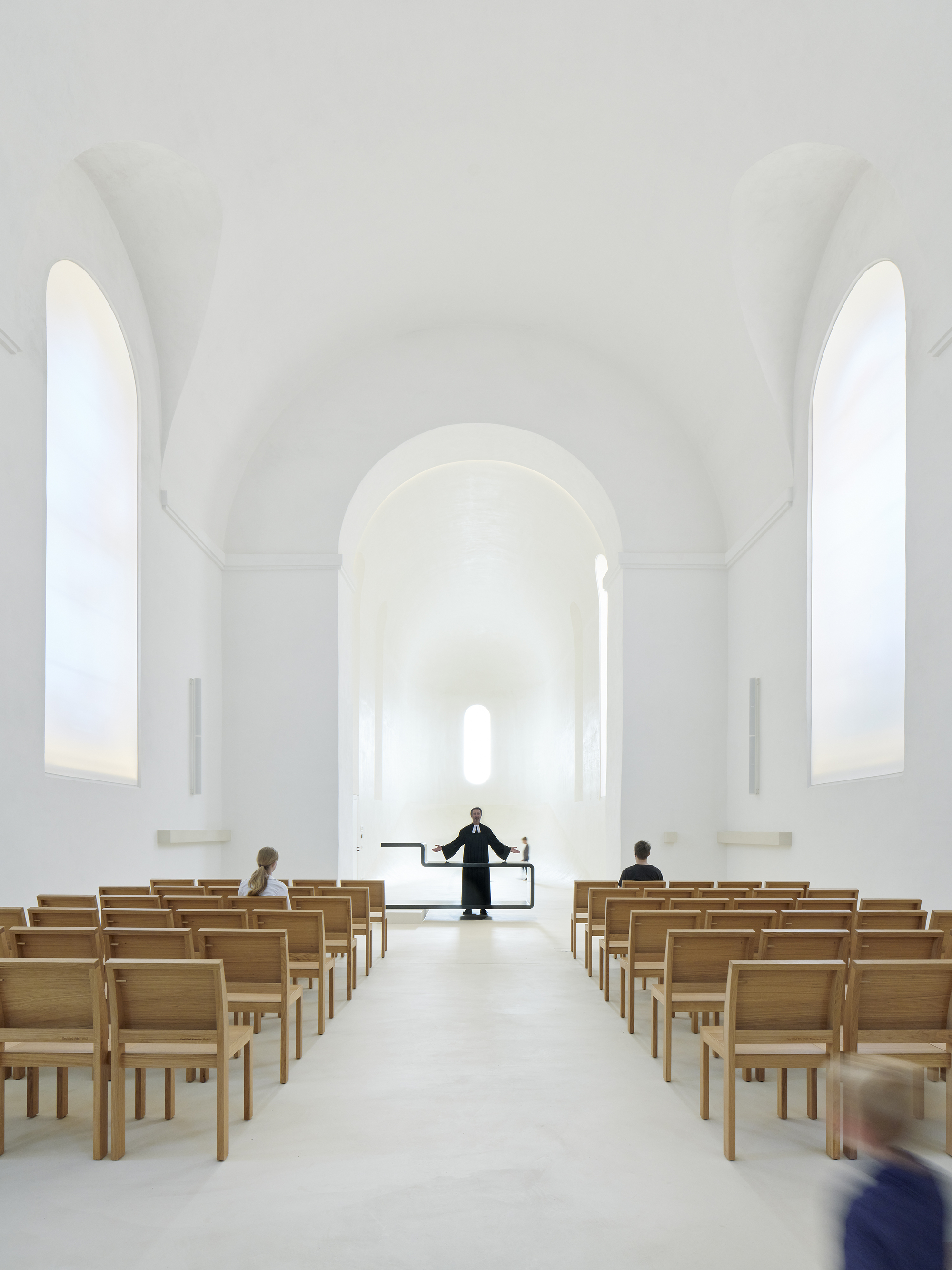 Whitewashed nave with barrel-vaulted ceiling, timber pews, and arched windows flooding the space with daylight