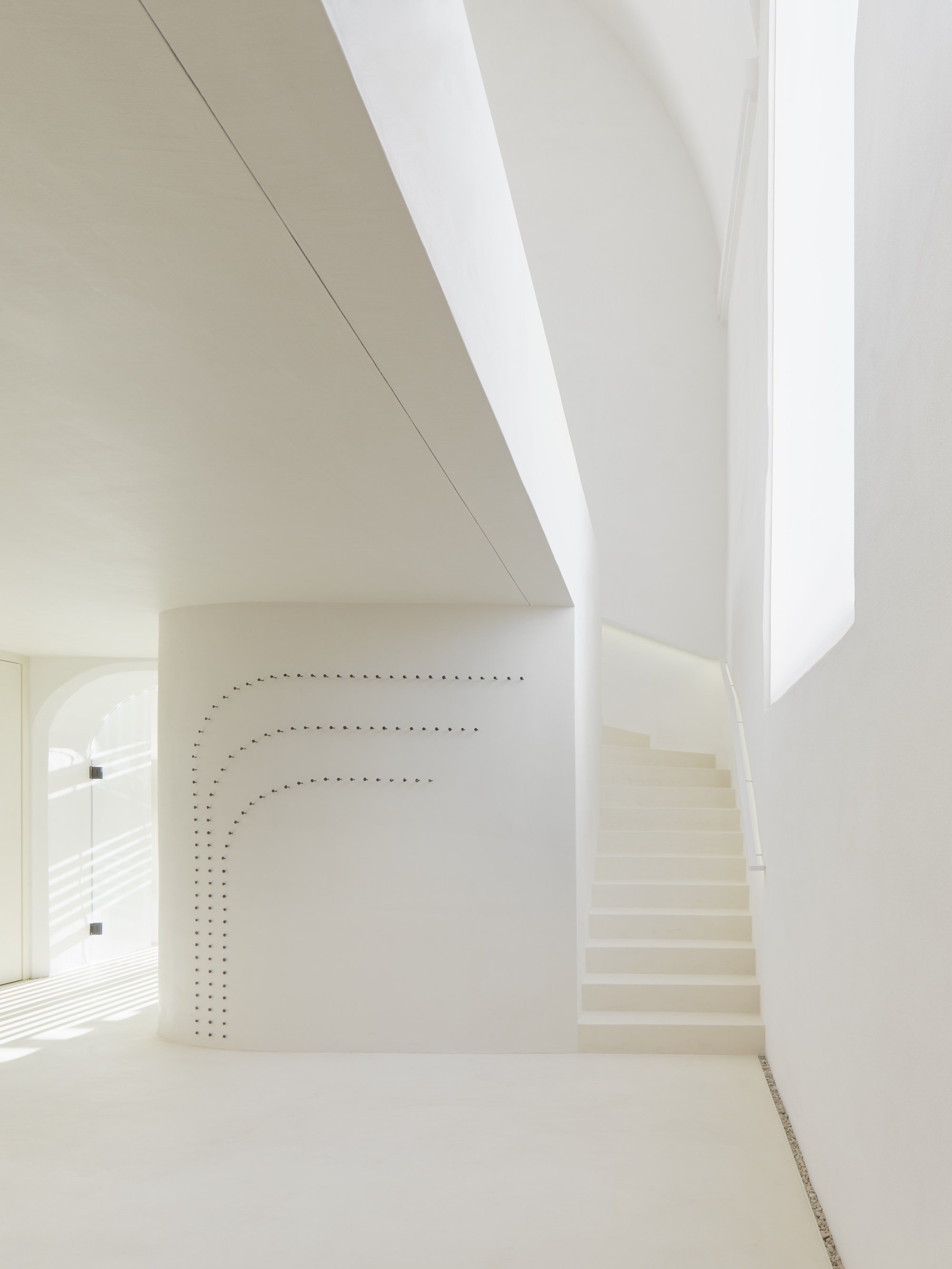 Curved white staircase ascending alongside a perforated wall beneath a skylight slit