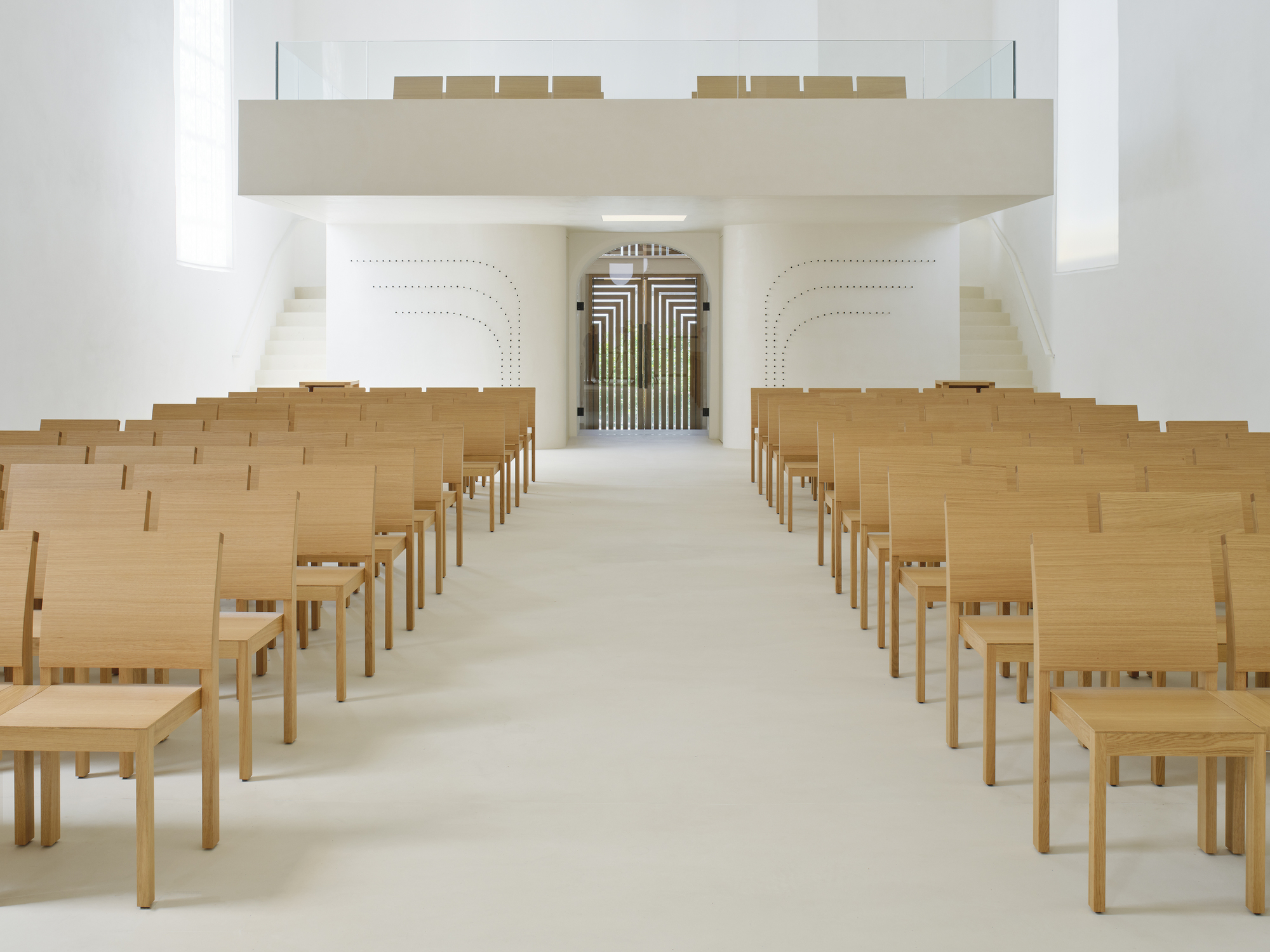 Rows of oak seating under cantilevered gallery facing perforated choir screen and organ pipes