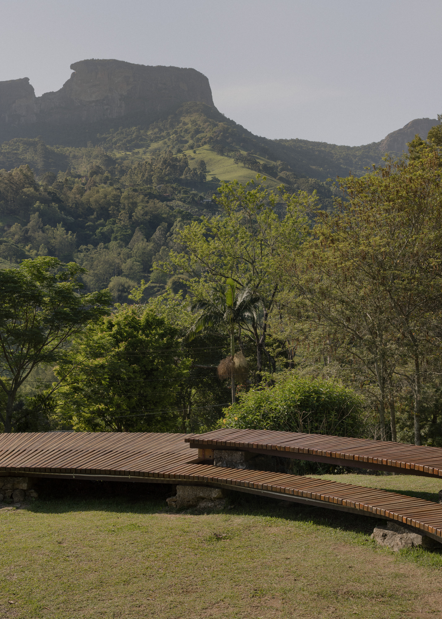 Slatted timber walkway extending across lawn beneath forested mountain ridge