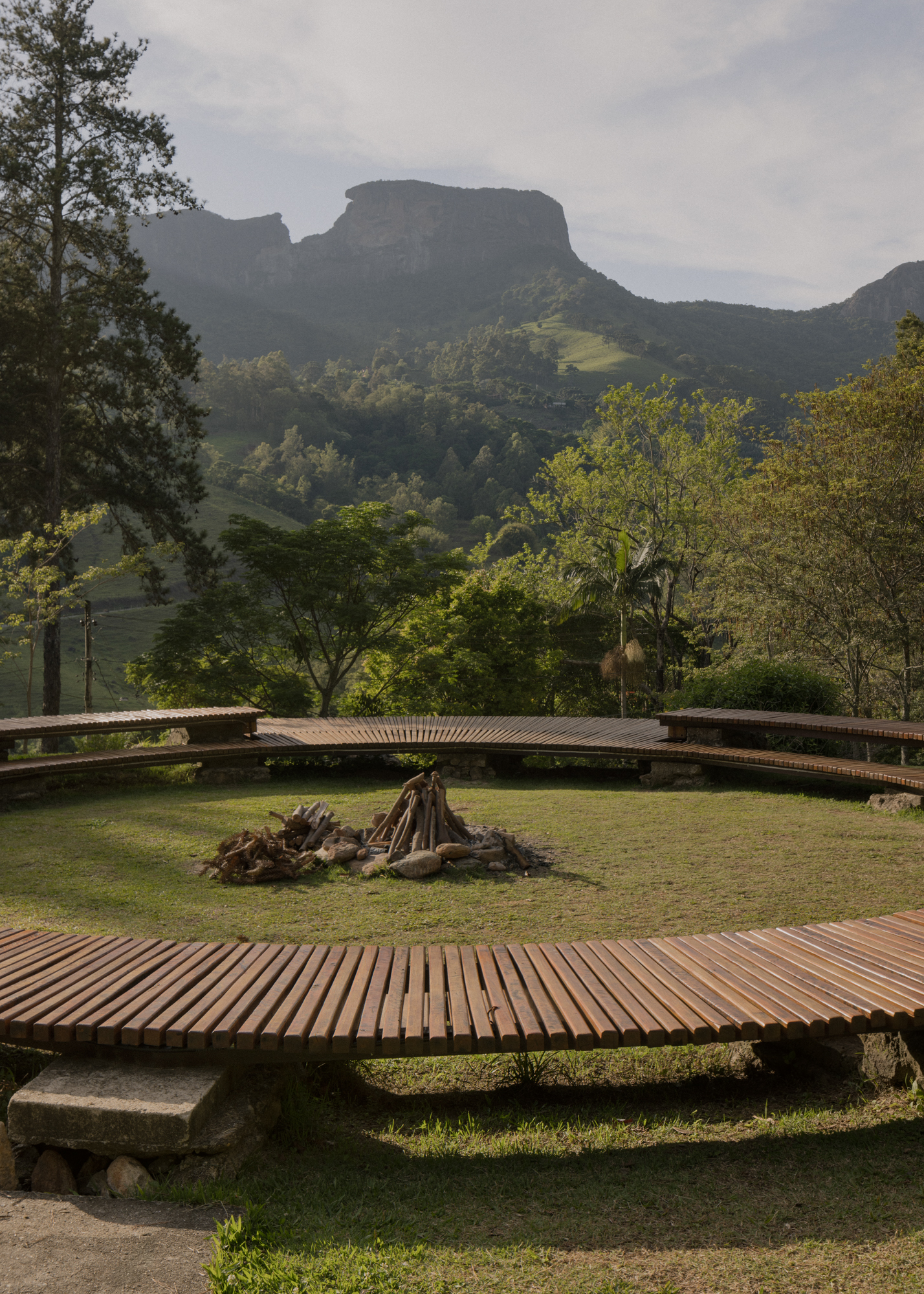 Circular timber deck platforms on grass with a central fire pit overlooking forested mountains