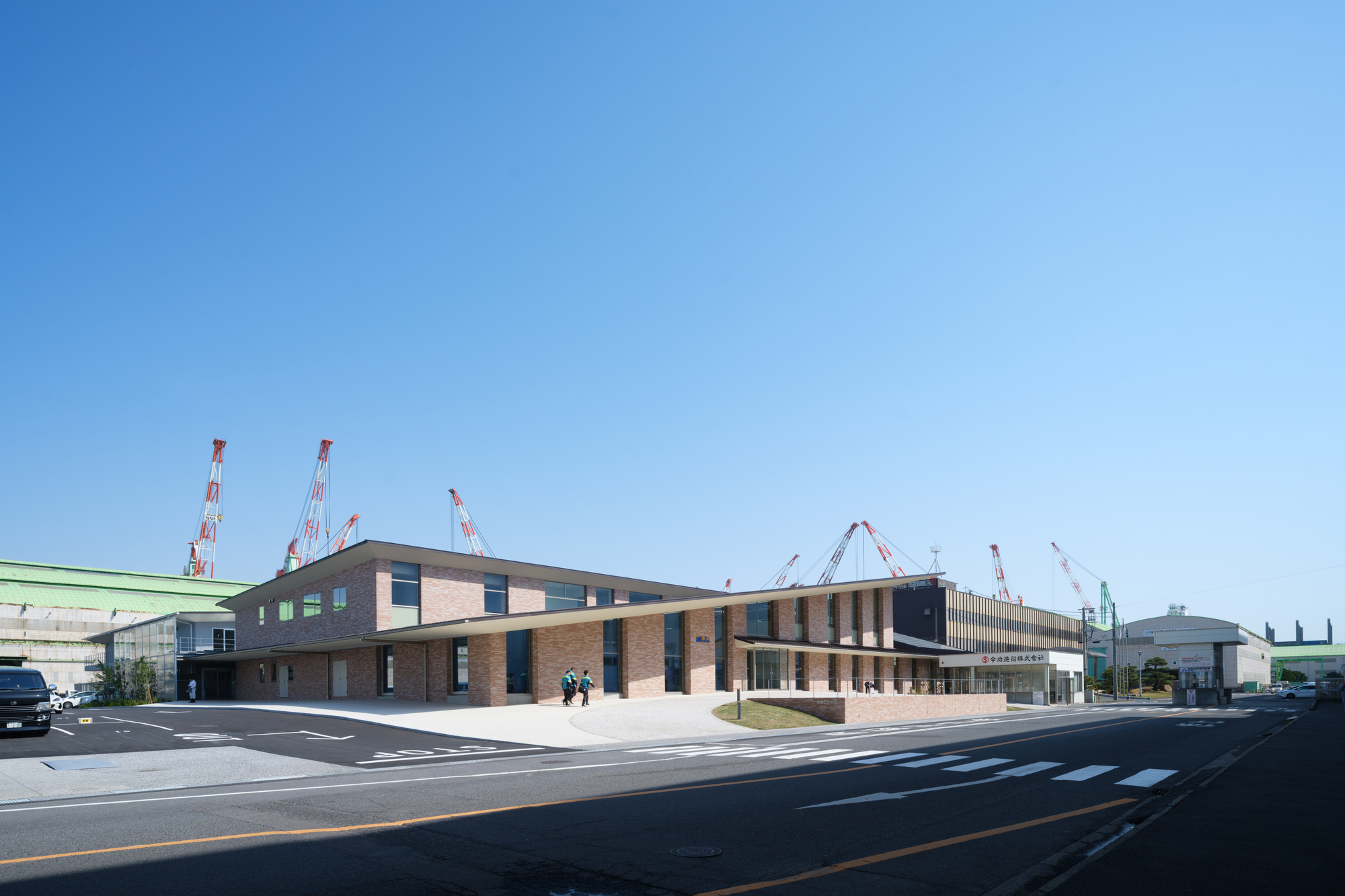 Long facade showing alternating brick volumes with vertical sunshades and pedestrians crossing at the entrance