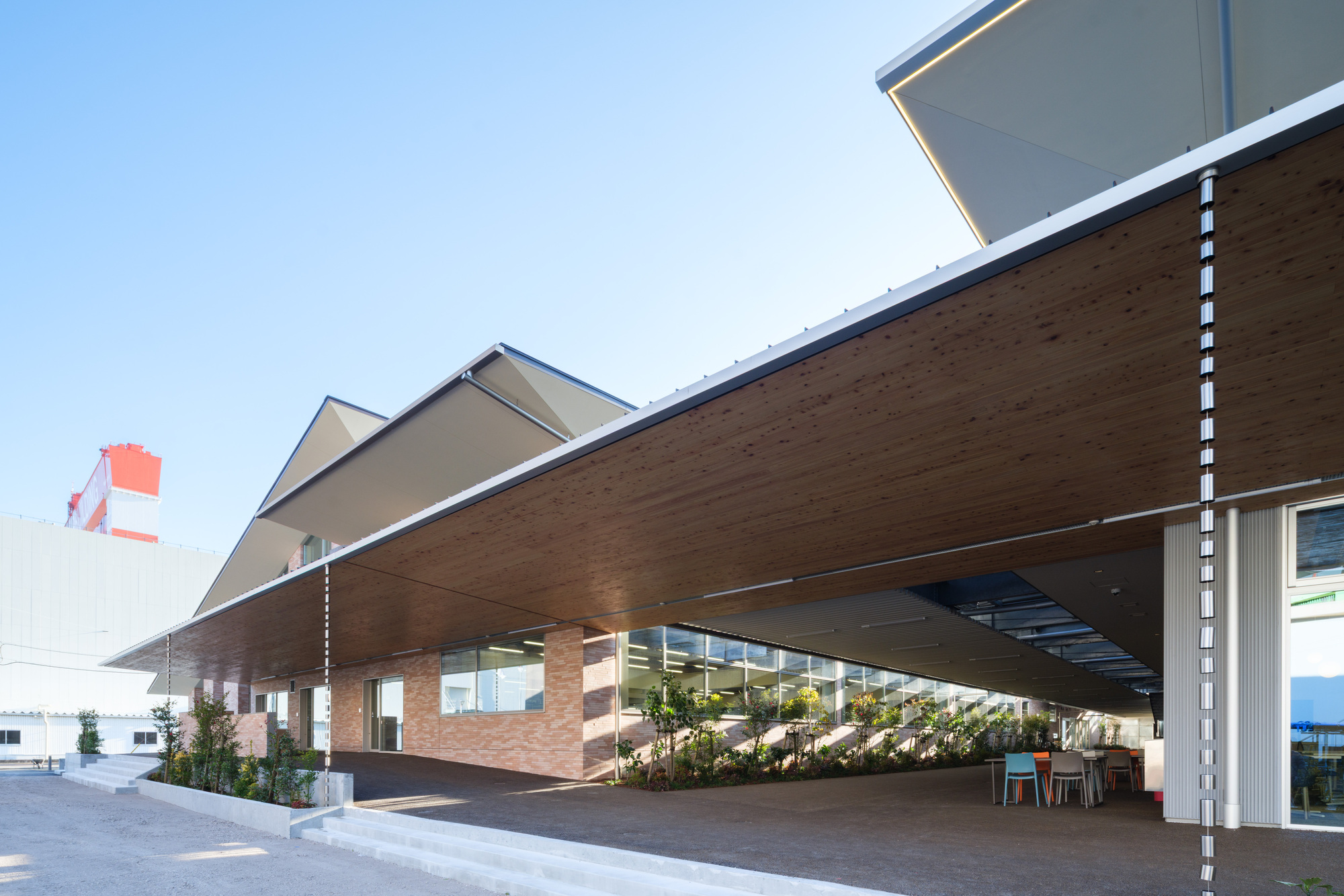 Covered drop-off canopy with timber soffit, brick columns, and planted beds under clear sky