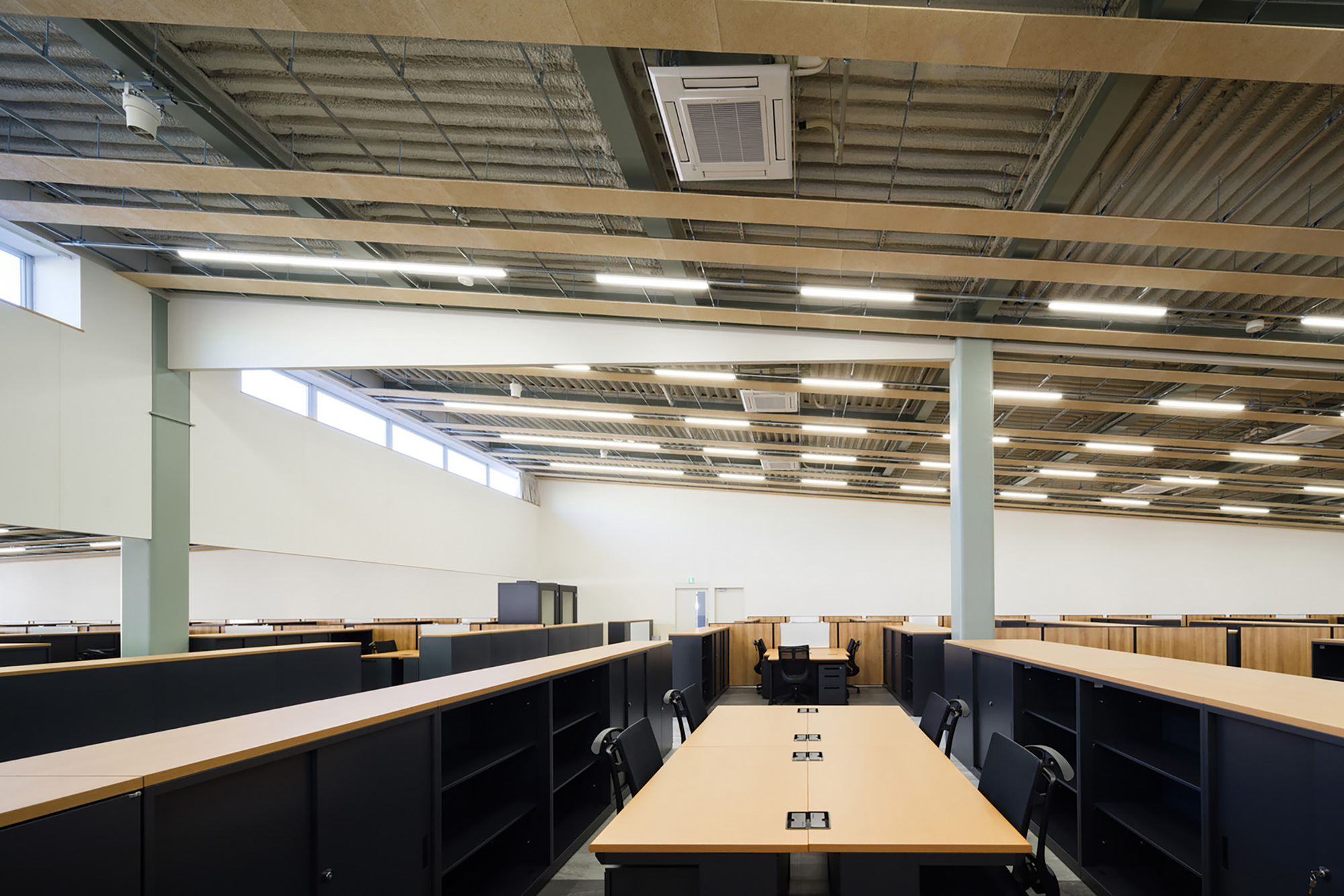 Open office workspace with exposed corrugated metal ceiling, linear lighting, and rows of black storage units