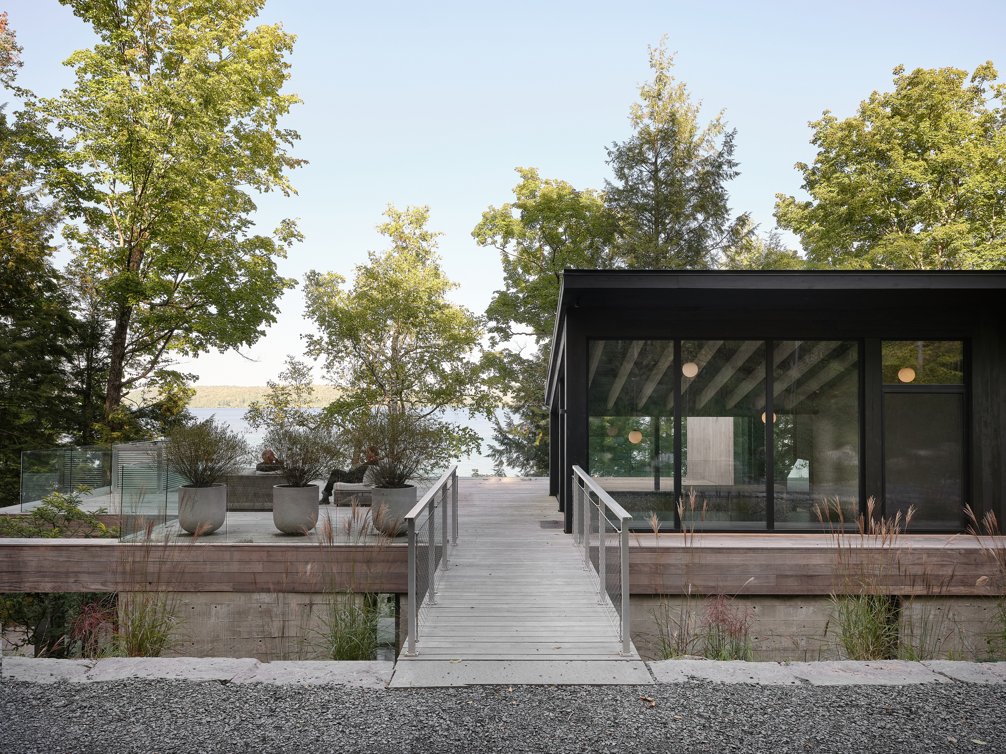 Timber boardwalk leading to a black glass pavilion with planted beds and deciduous trees