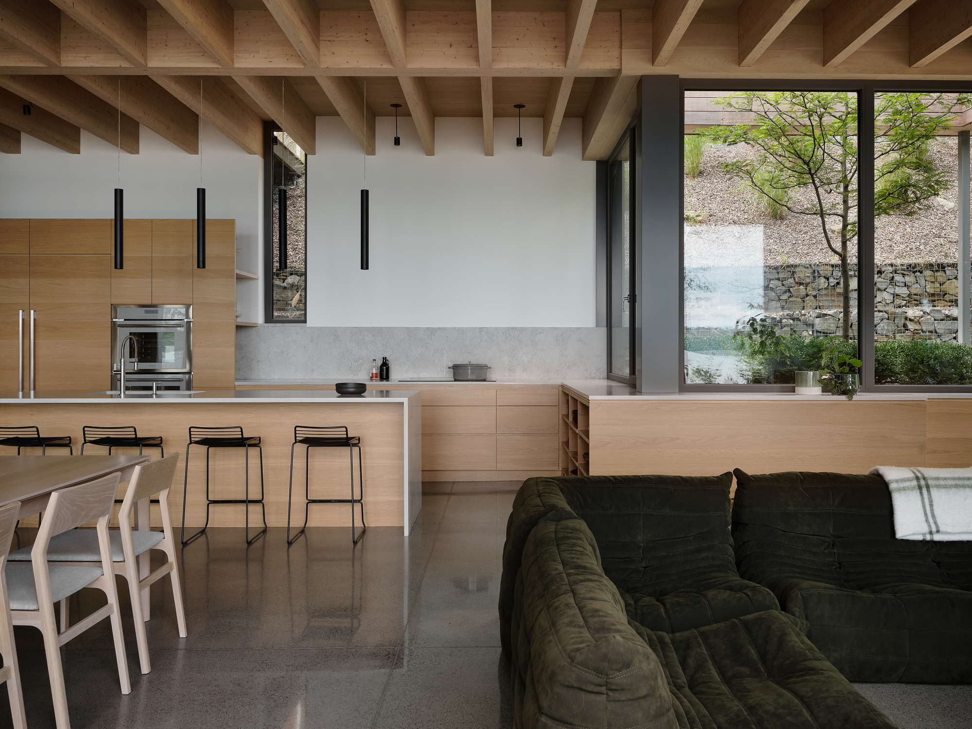 Open-plan kitchen and living space with exposed timber ceiling joists and polished concrete floor