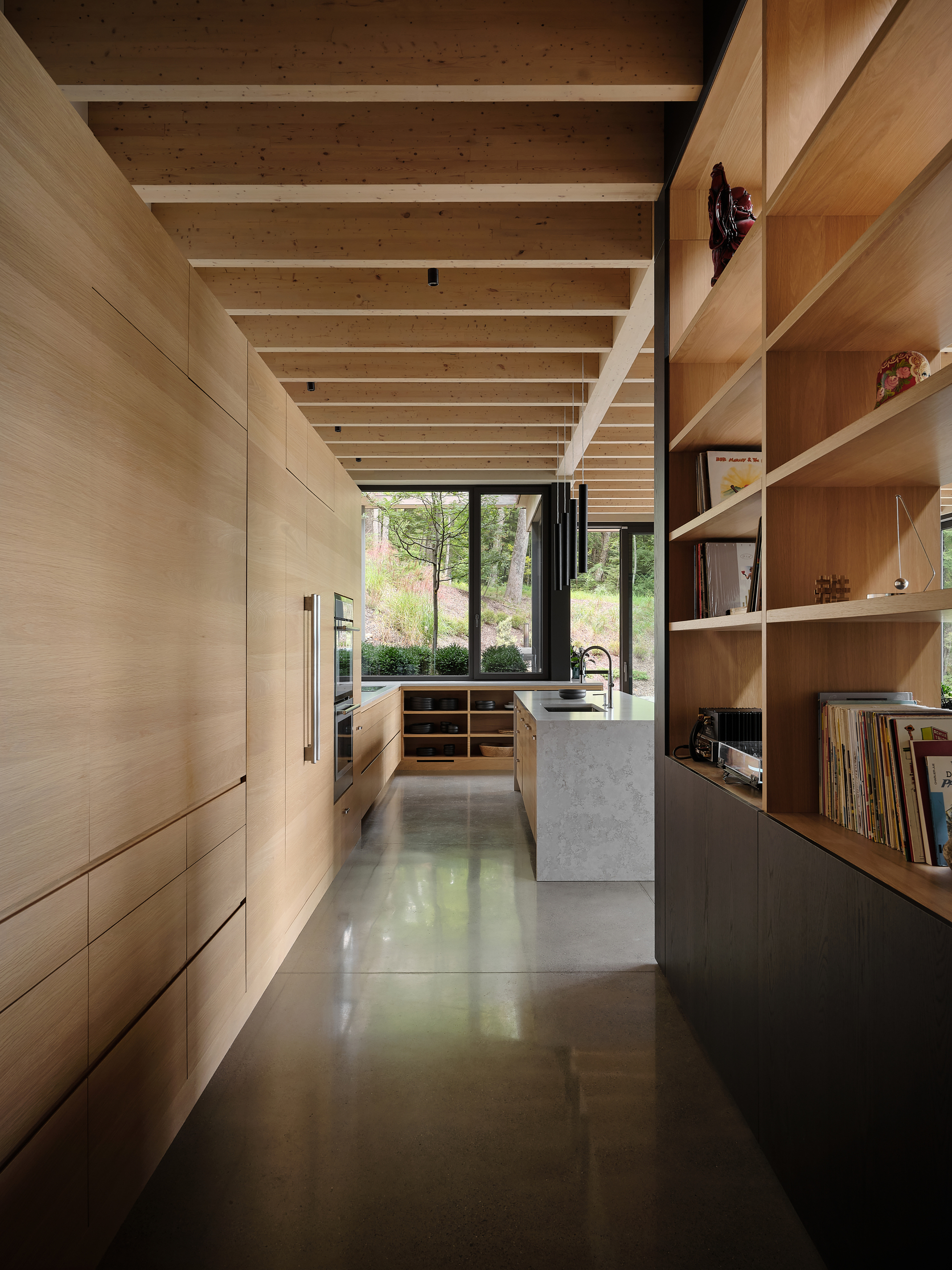 Galley hallway with open timber shelving and concrete flooring beneath a rhythmic exposed beam ceiling