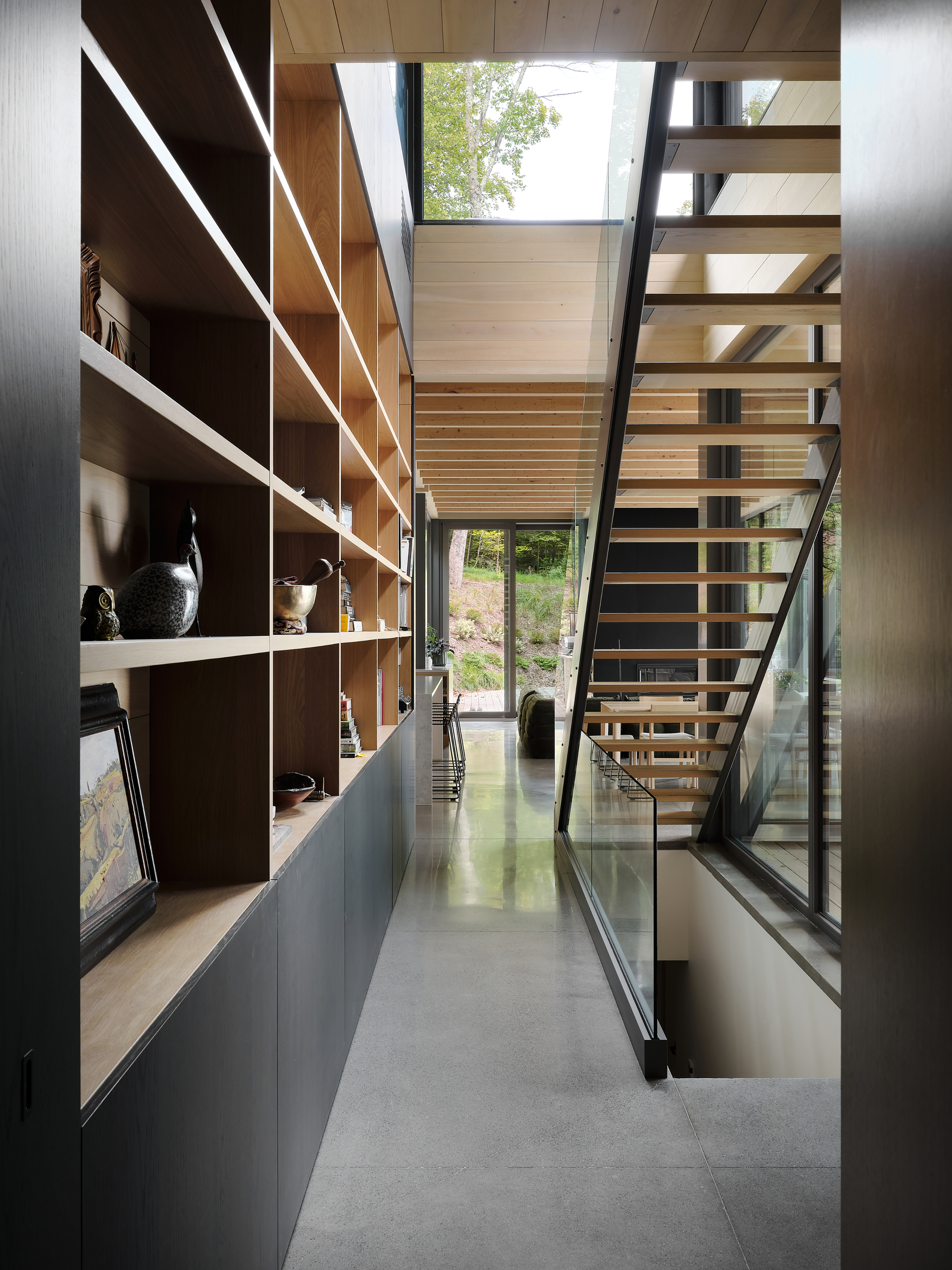 Narrow corridor with open-tread timber stair alongside built-in shelving illuminated by natural light from above