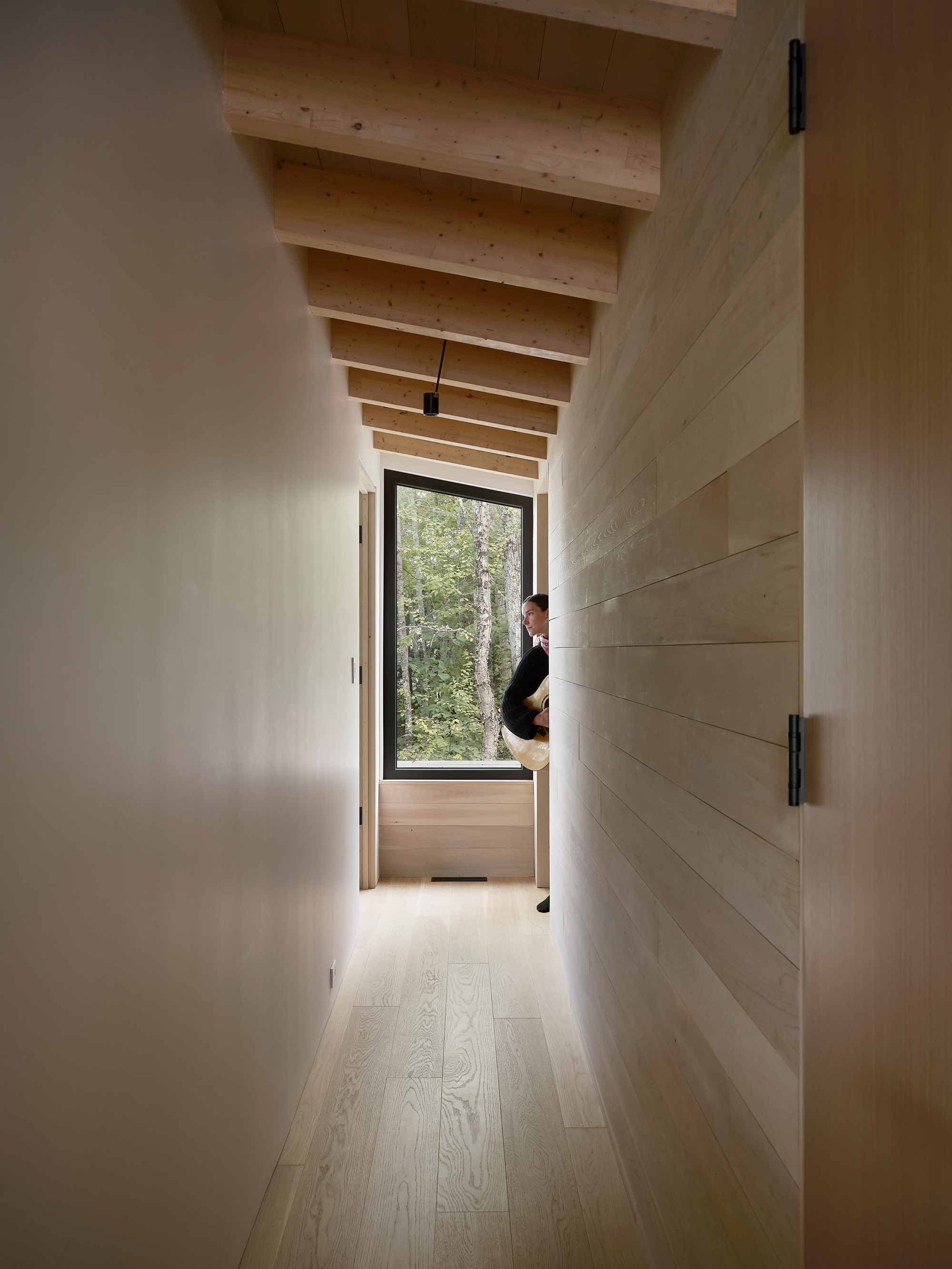 Corridor with exposed timber joists overhead leading to a window seat where a person sits looking out