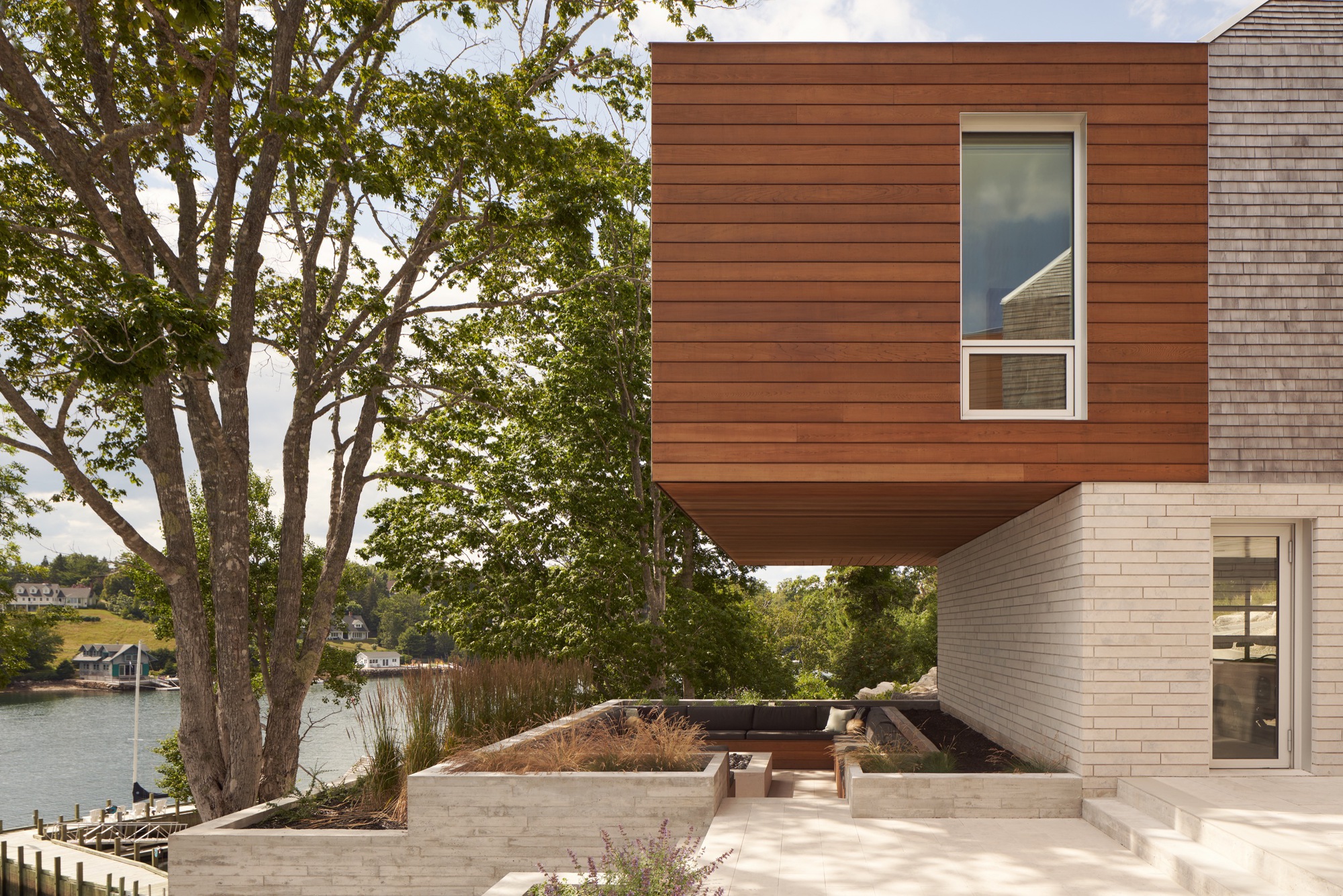 Cantilevered wood-clad box above a limestone base and waterside planting beds with lake beyond