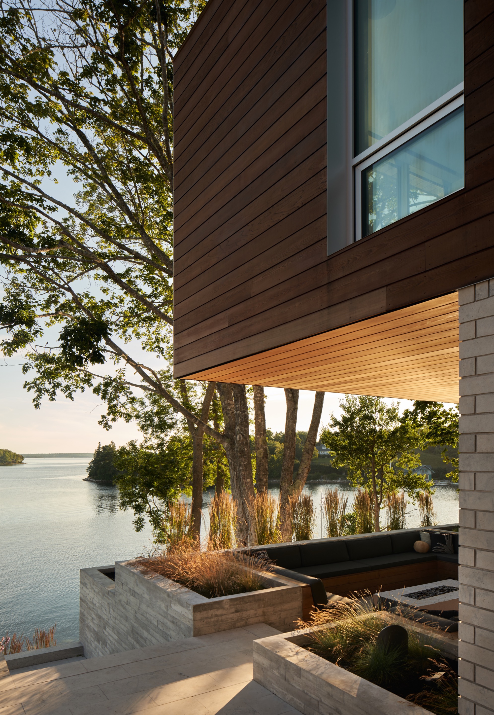Cantilevered wood soffit above planted concrete beds with ornamental grasses facing the lake at dusk