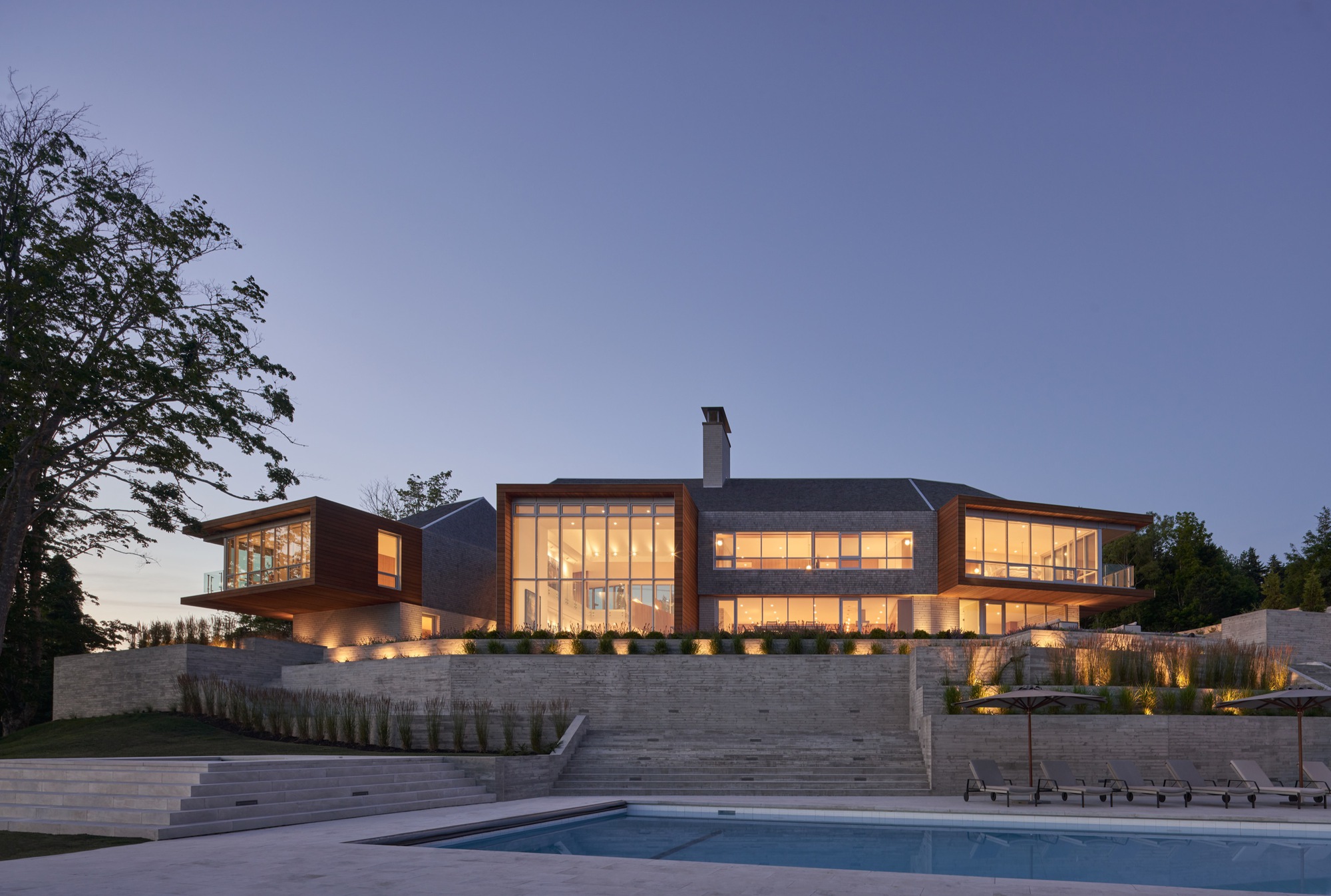 Night view of the illuminated glass facades with uplighting along limestone terraces beside the pool