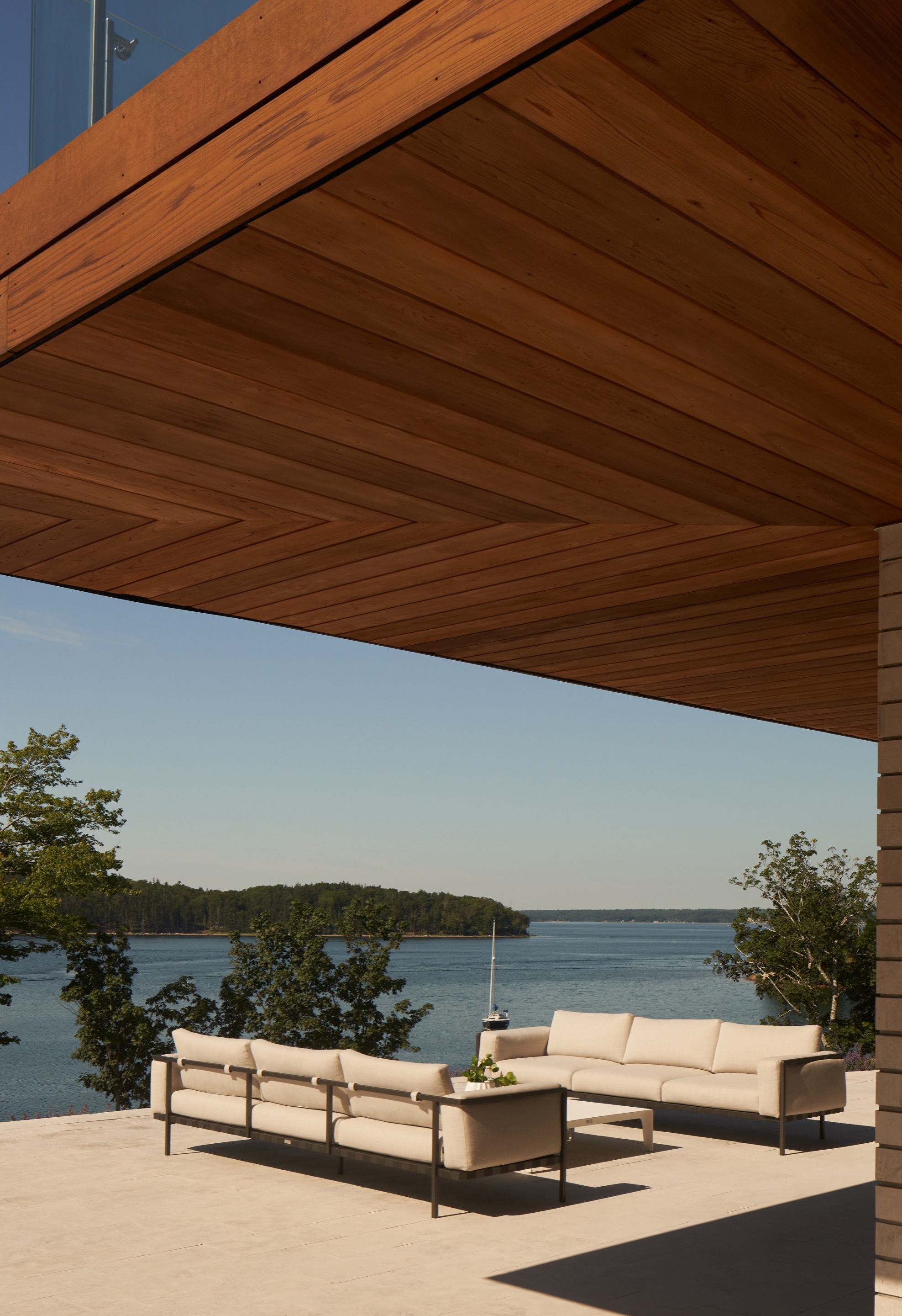 Covered terrace with timber ceiling and outdoor seating overlooking a forested lake in clear daylight